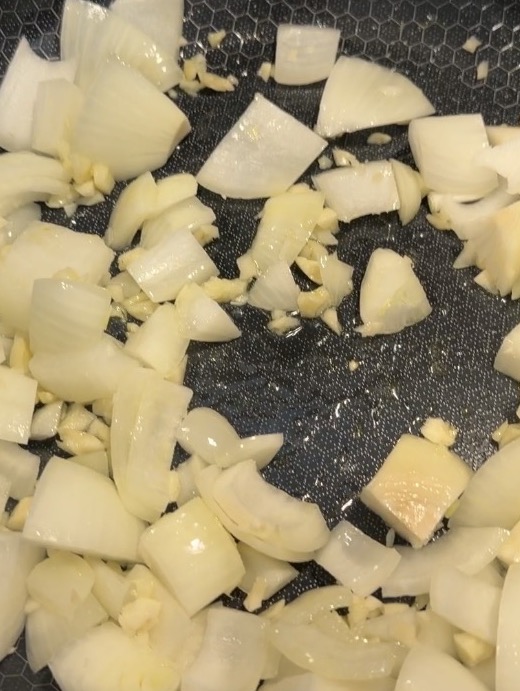 Chopped onions and minced garlic sautéing in a pan.