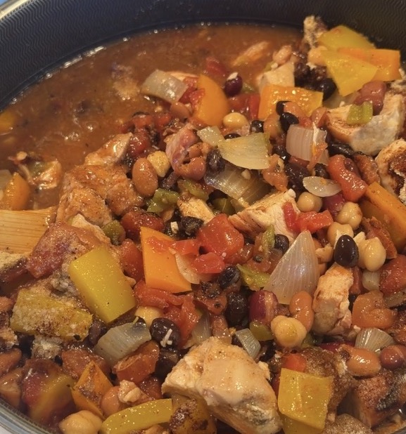 A skillet filled with a stew of chicken, black beans, chickpeas, bell peppers, onions, and tomatoes.