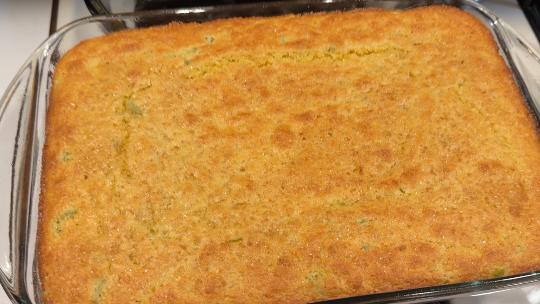 A freshly baked rectangular pan of cornbread with visible green bits inside.