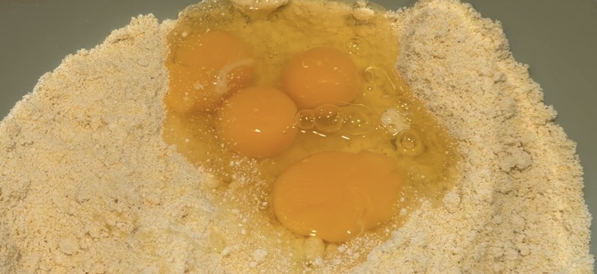 Three raw eggs cracked into a bowl of dry flour.