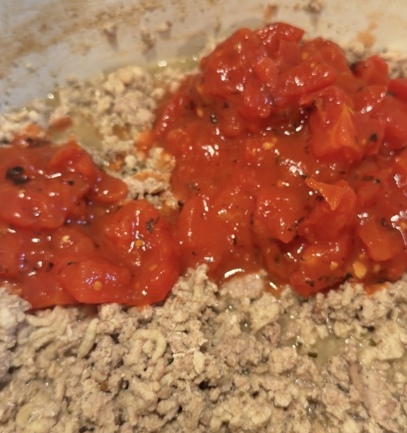 Diced canned tomatoes added to a pan of cooked ground meat.