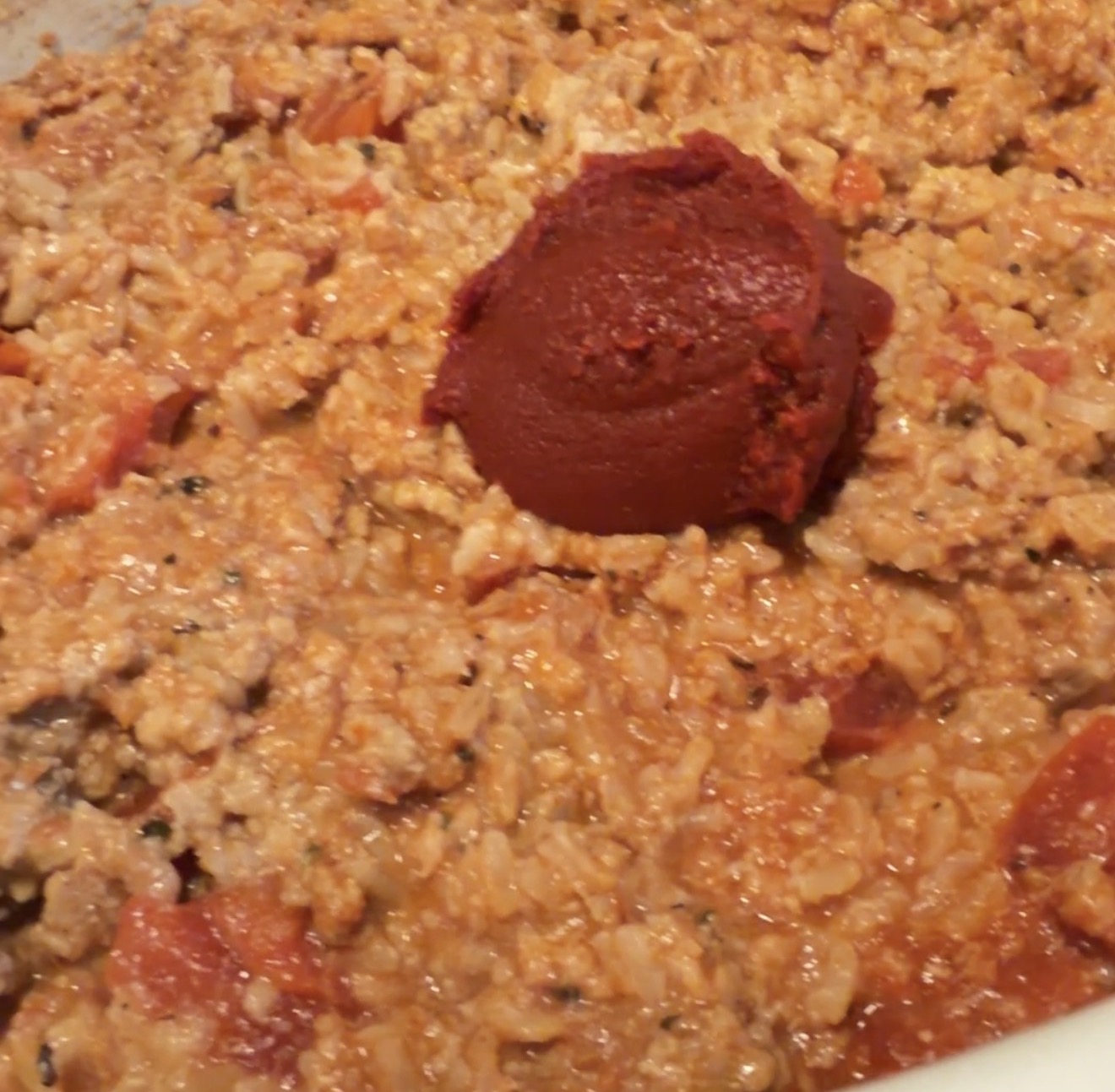 A dollop of thick tomato paste centered on a pan of cooked ground meat and rice mixture.
