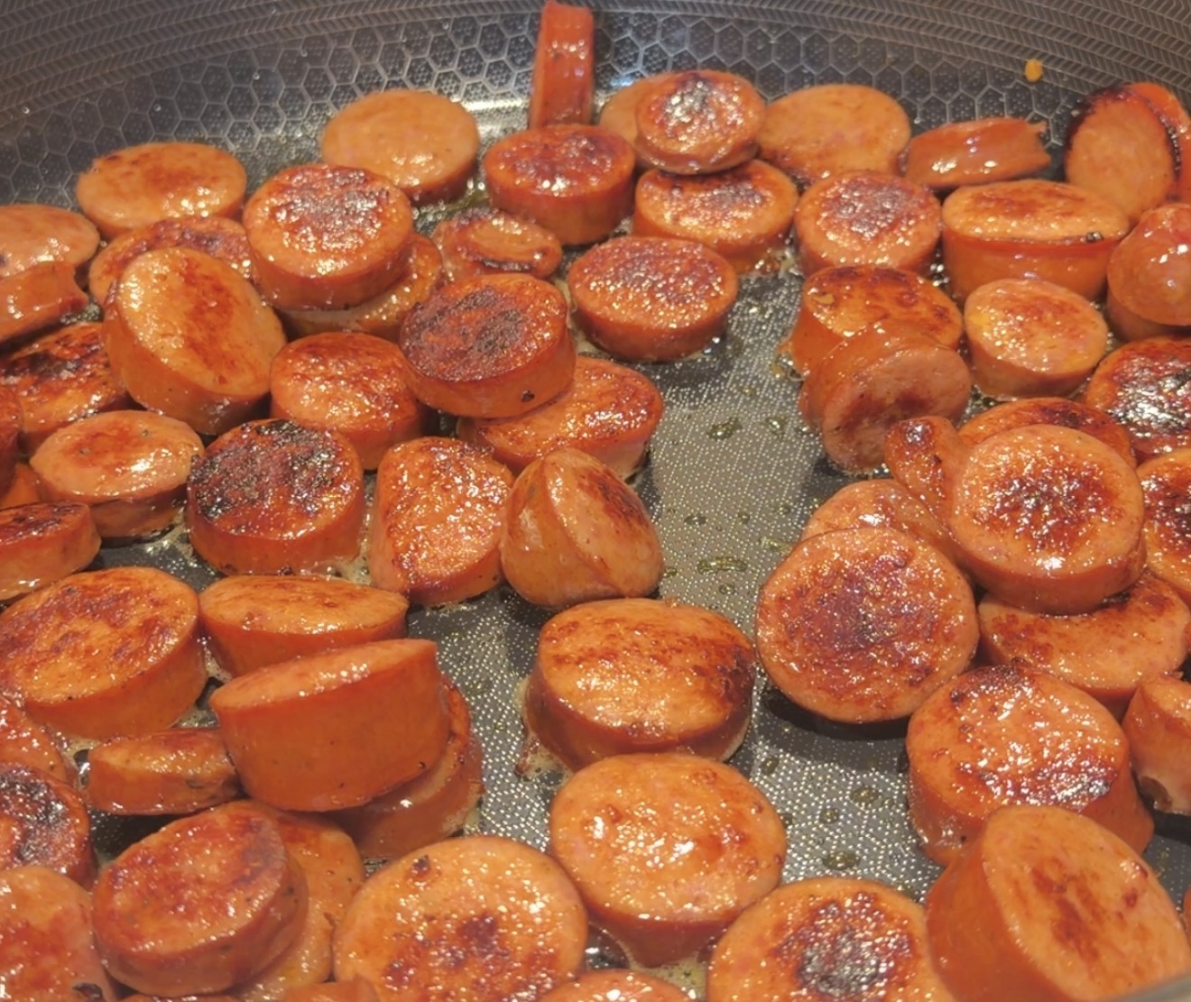 Sliced sausage coins frying in a pan.