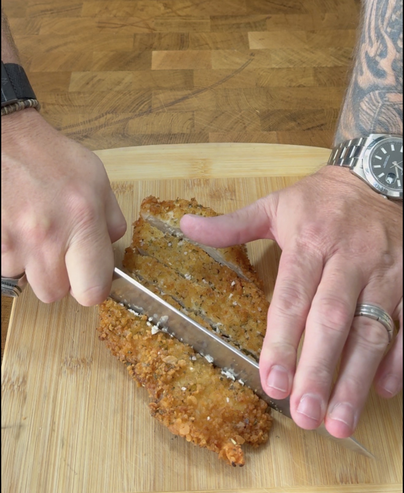 A person slicing a breaded fried chicken cutlet on a wooden cutting board.