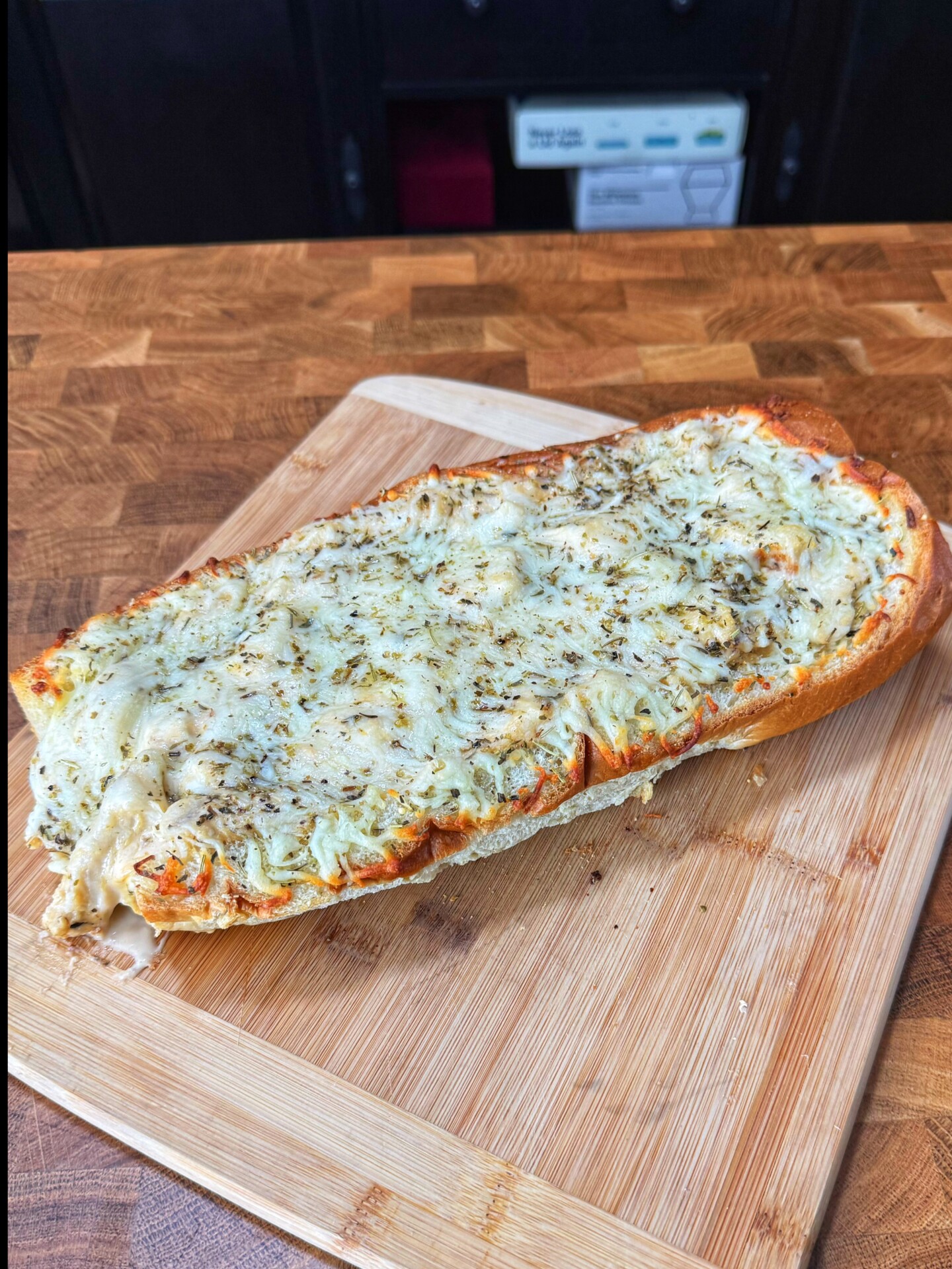 French bread pizza topped with melted cheese and herbs on a wooden cutting board.