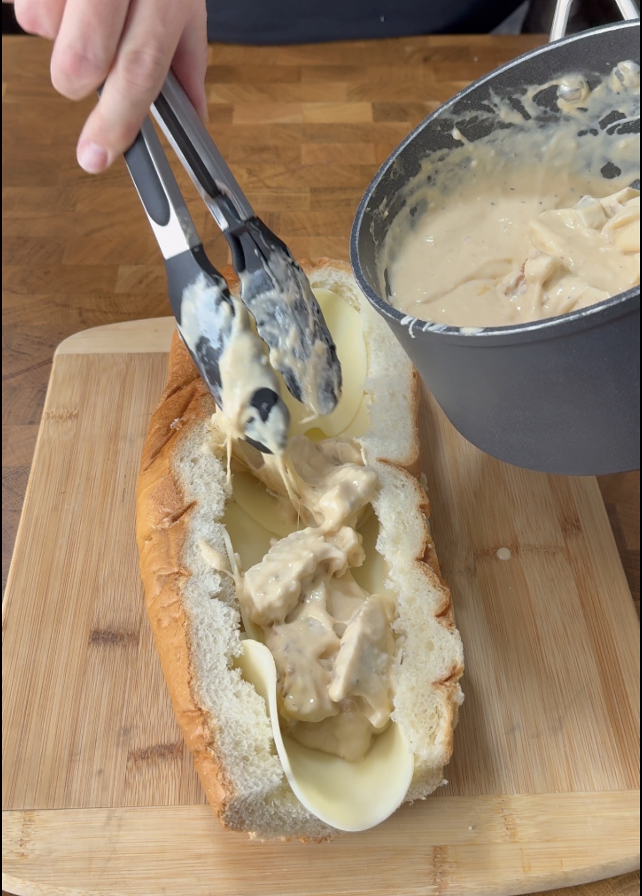 Tongs place creamy chicken mixture from a saucepan onto sliced bread lined with cheese.