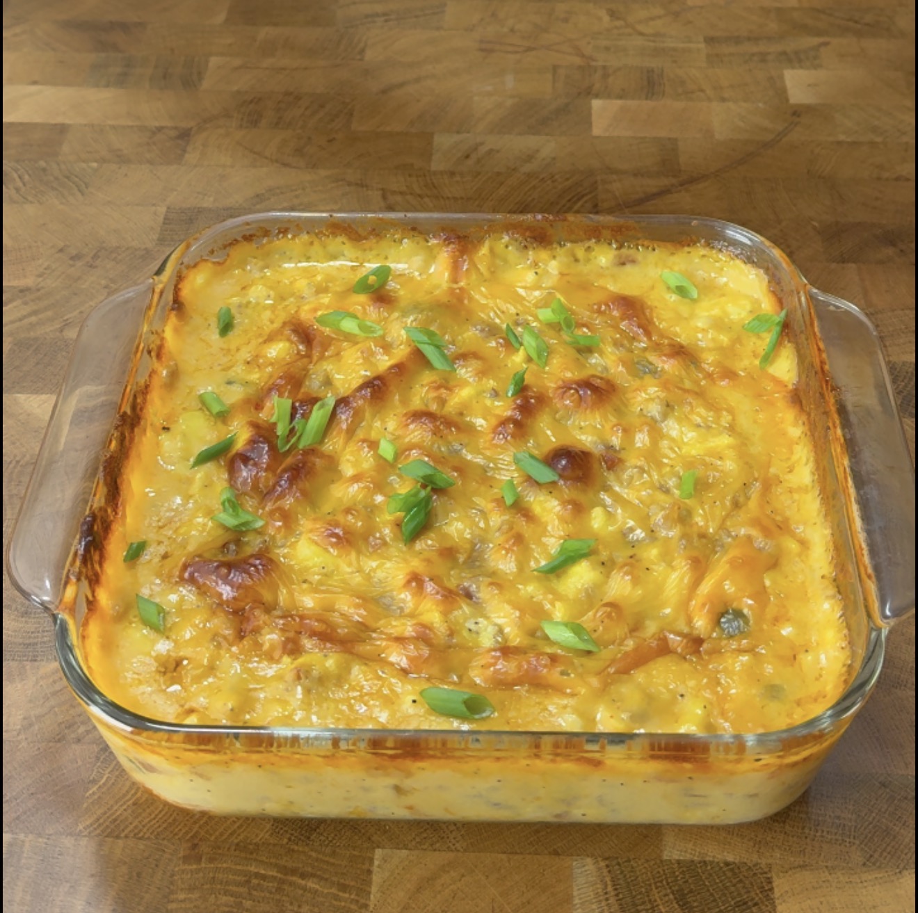 A square glass baking dish filled with a baked cheesy casserole topped with sliced green onions.