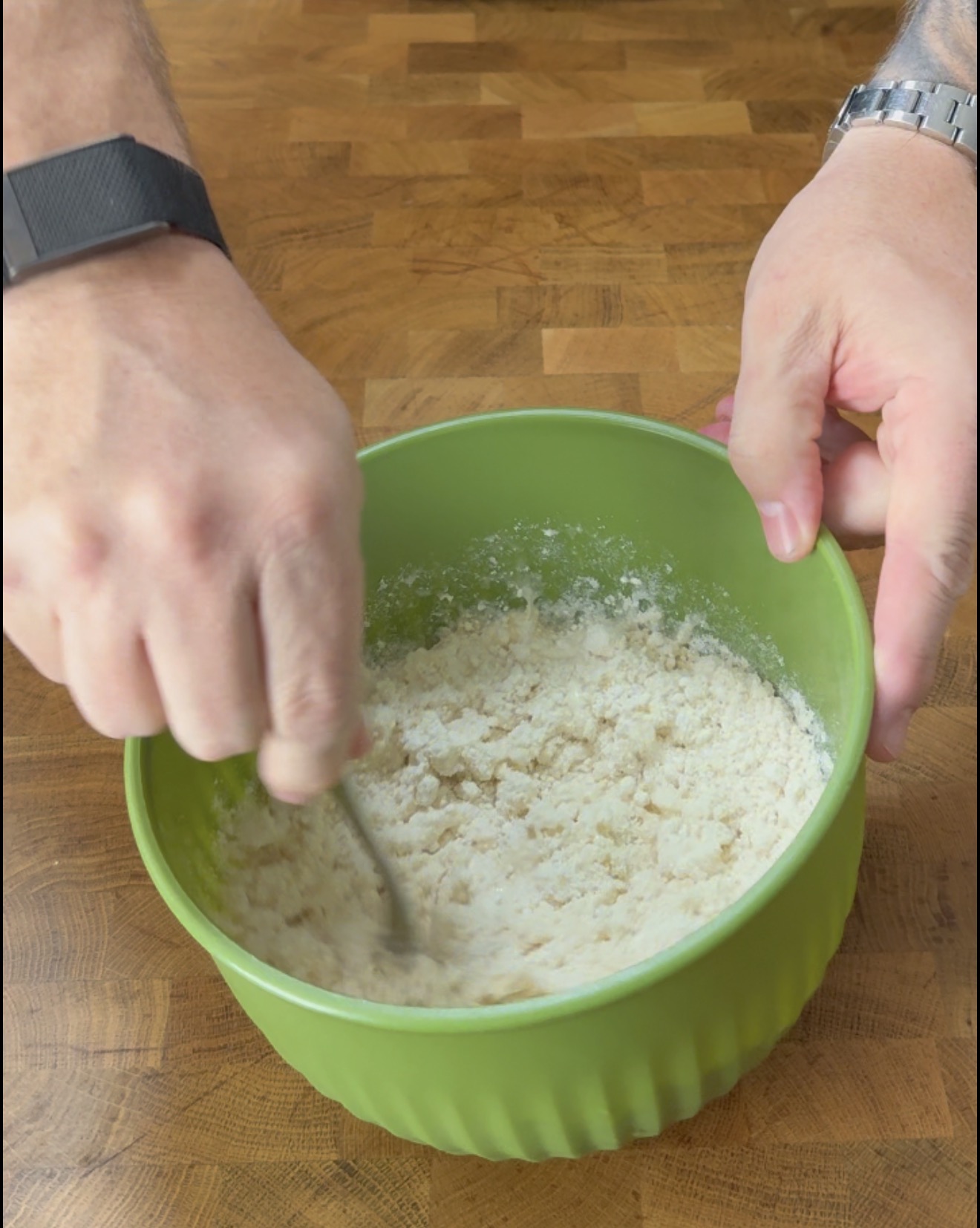 A persons hands using a fork to mix ingredients in a green bowl.