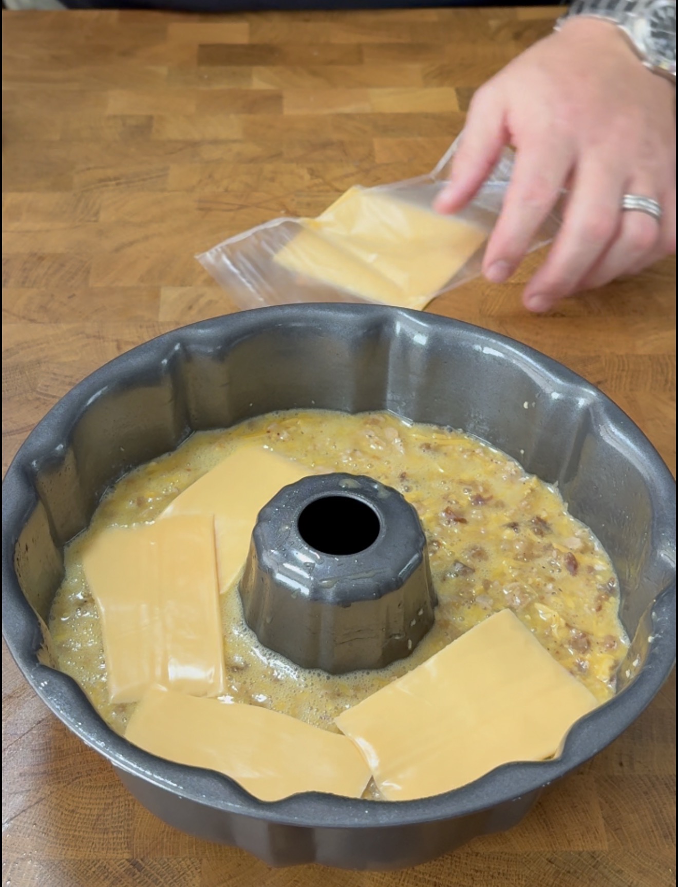 A person placing slices of cheddar cheese onto an egg and sausage mixture in a bundt pan.