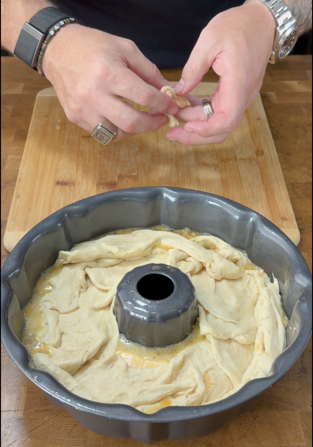 Hands placing pieces of dough into a greased bundt pan on a wooden board.