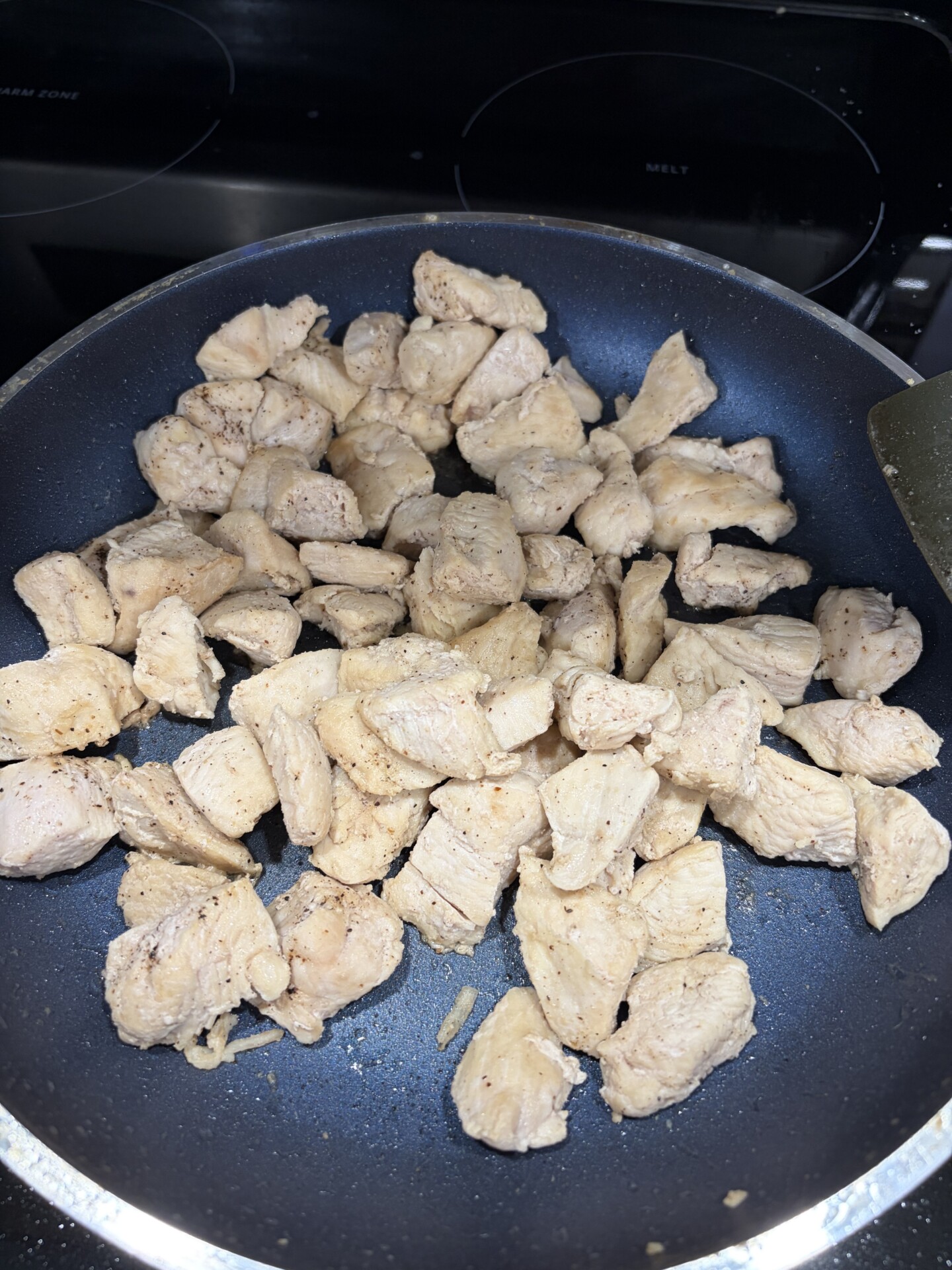 Cubed pieces of seasoned chicken cooking in a black nonstick frying pan on a stovetop.