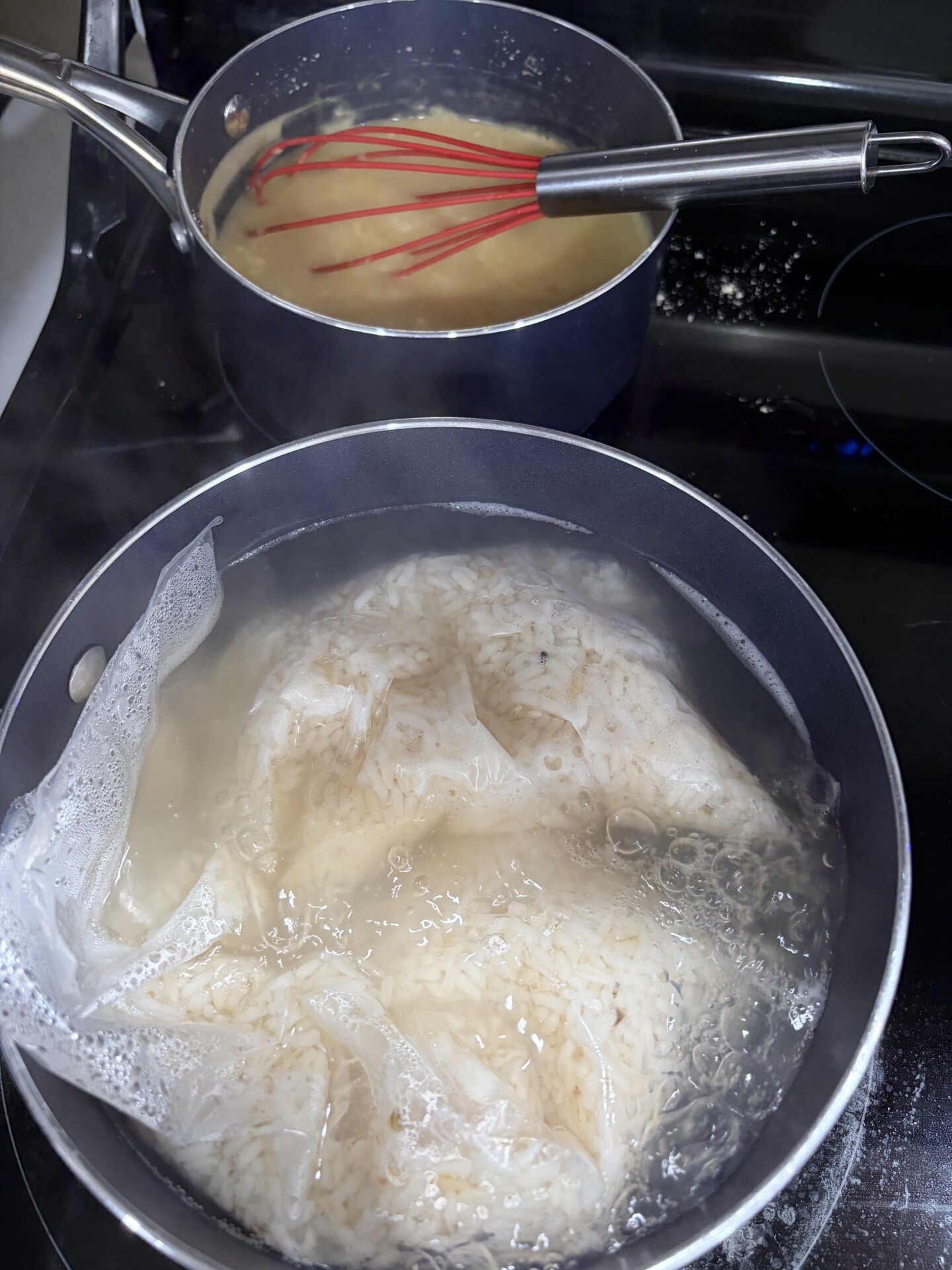 A pot of rice boiling in a mesh bag is on the stove in front, and a second pot with a whisk and yellow liquid is cooking behind it. Steam rises from the pots.