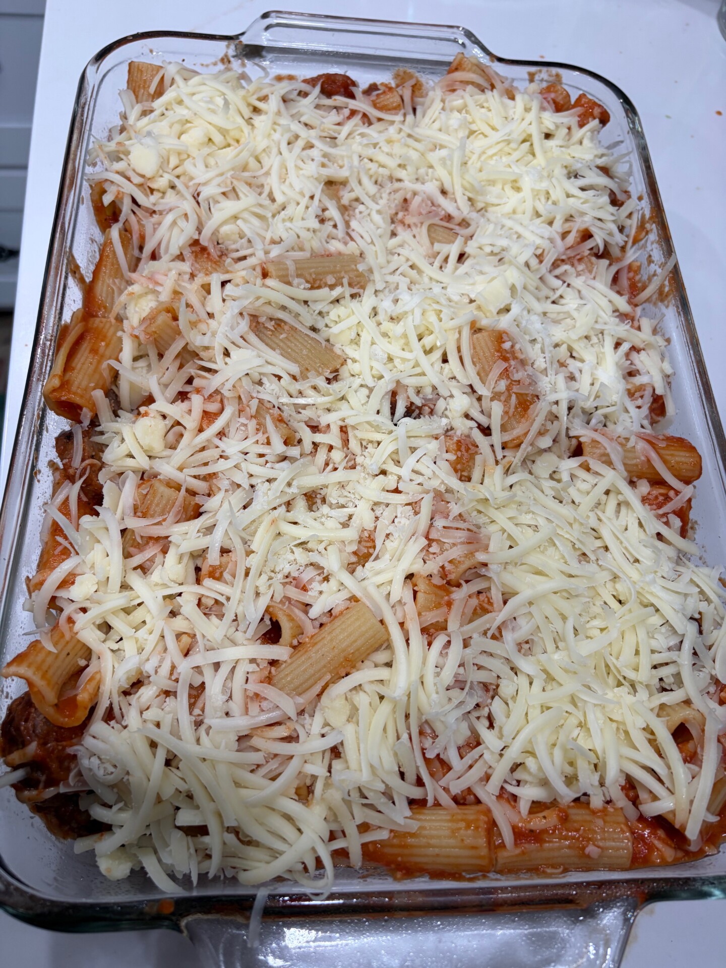 A glass baking dish filled with uncooked baked ziti pasta, topped with shredded mozzarella cheese, ready to be baked.