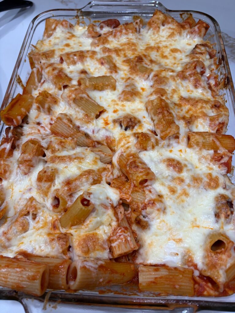 Baked rigatoni pasta in a glass dish, topped with melted mozzarella cheese and tomato sauce, with the cheese golden and bubbly.