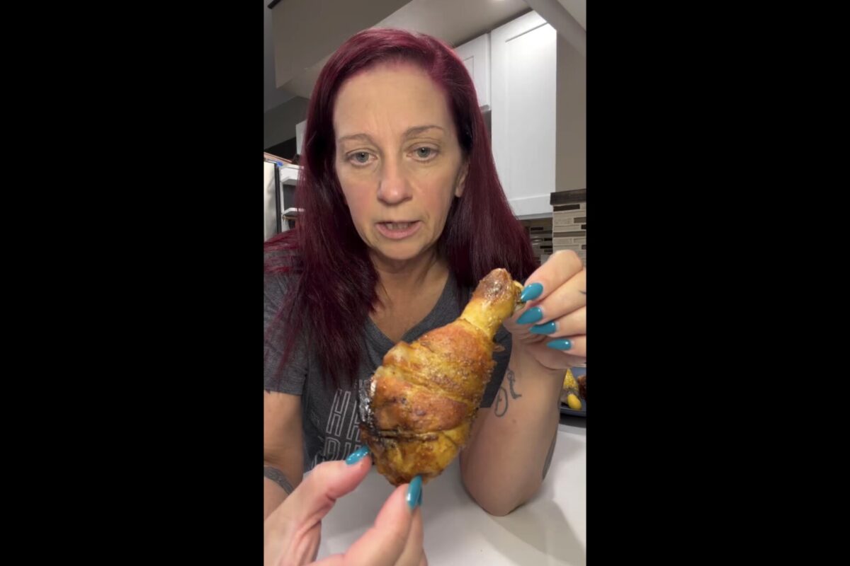 A woman holds up a cooked chicken drumstick for the camera.