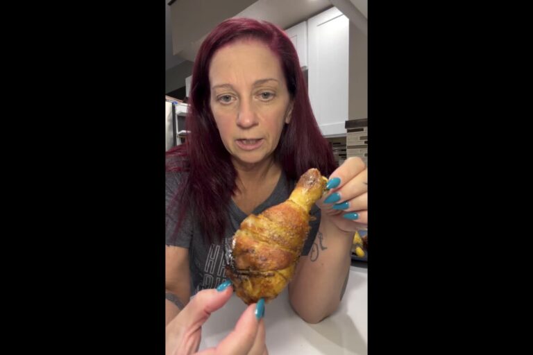 A woman holds up a cooked chicken drumstick for the camera.