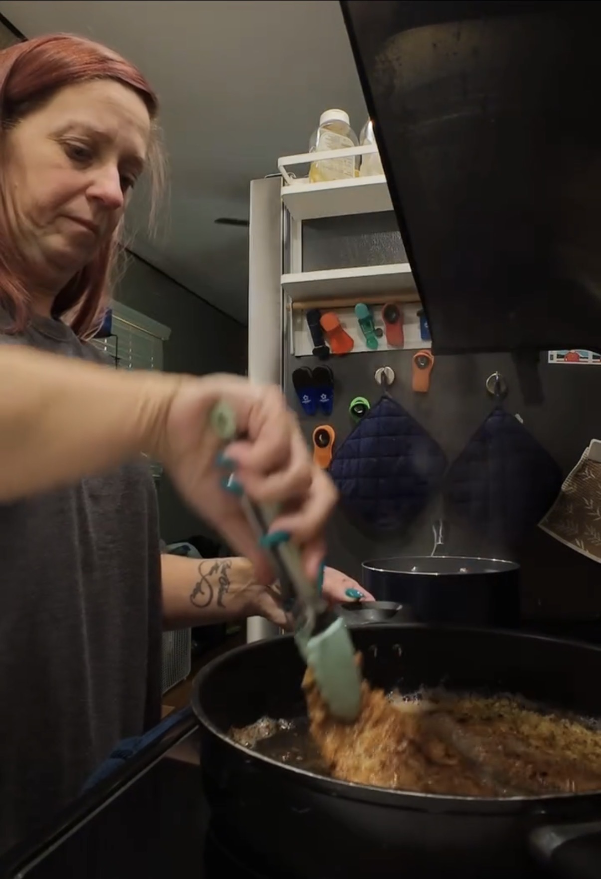 A woman cooking in a pan on a stovetop with tongs.