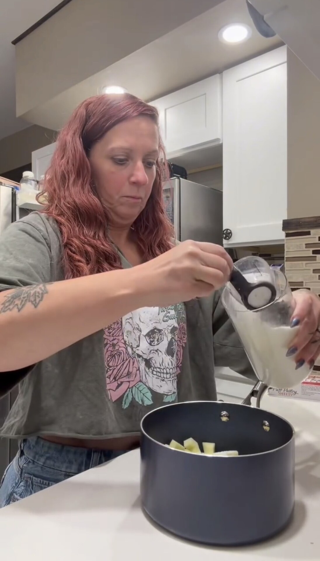 A person pouring milk from a measuring cup into a saucepan containing chopped fruit.