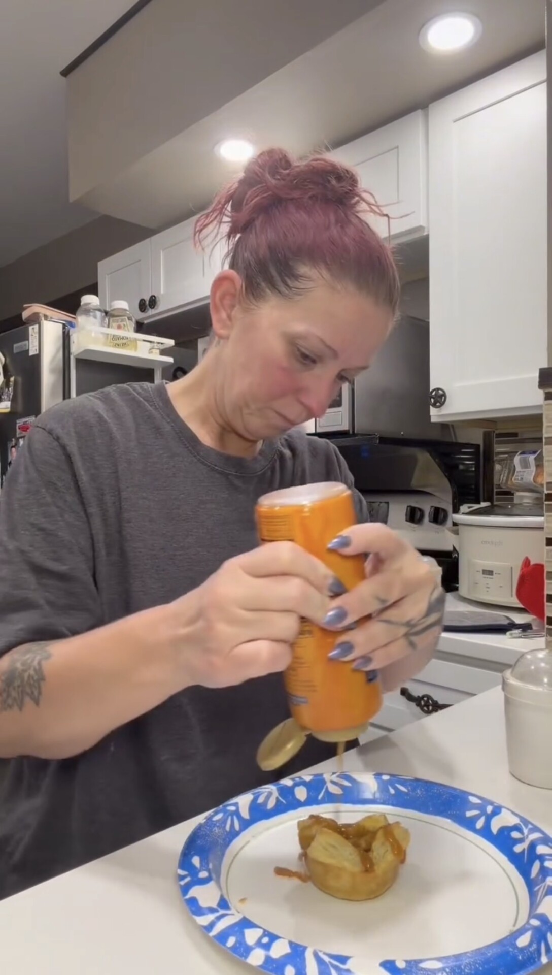 A person in a kitchen drizzling syrup onto a small pastry on a blue patterned plate.