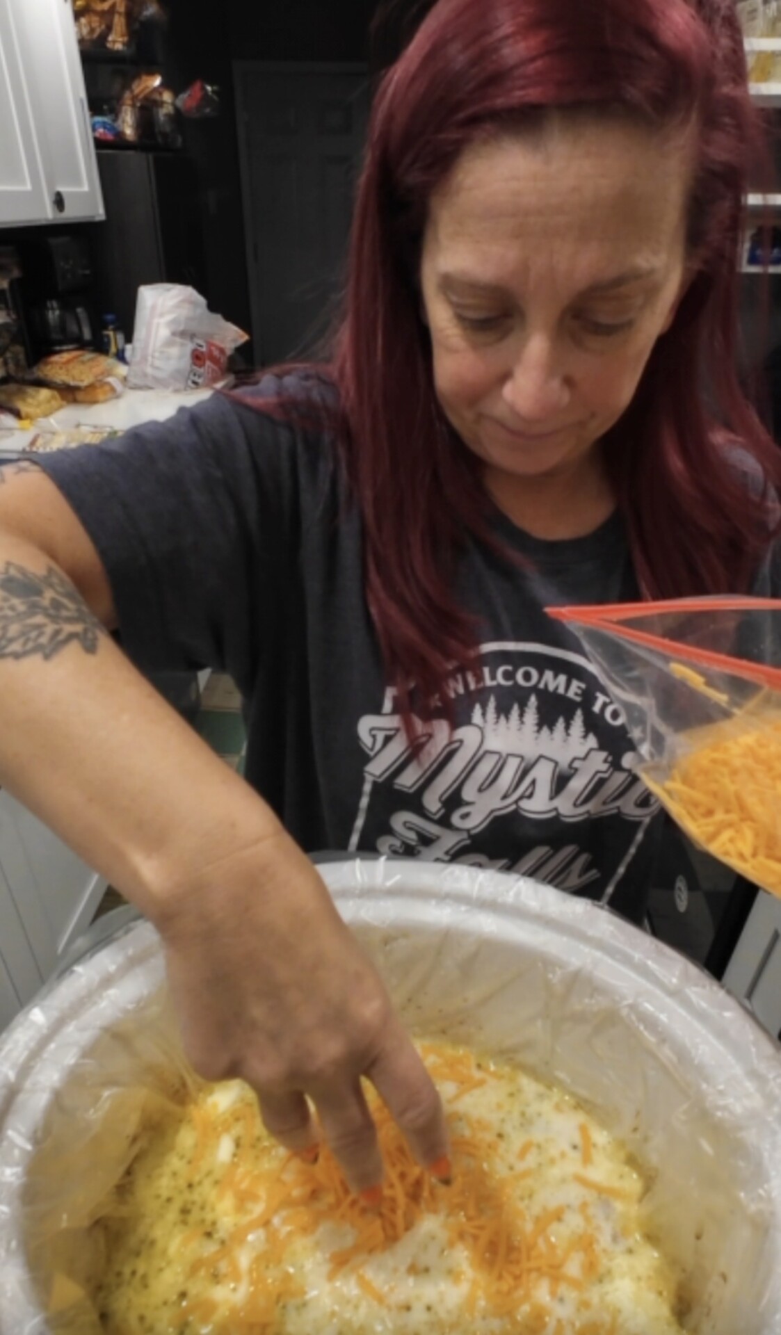 A person sprinkles shredded cheese from a plastic bag into a slow cooker.