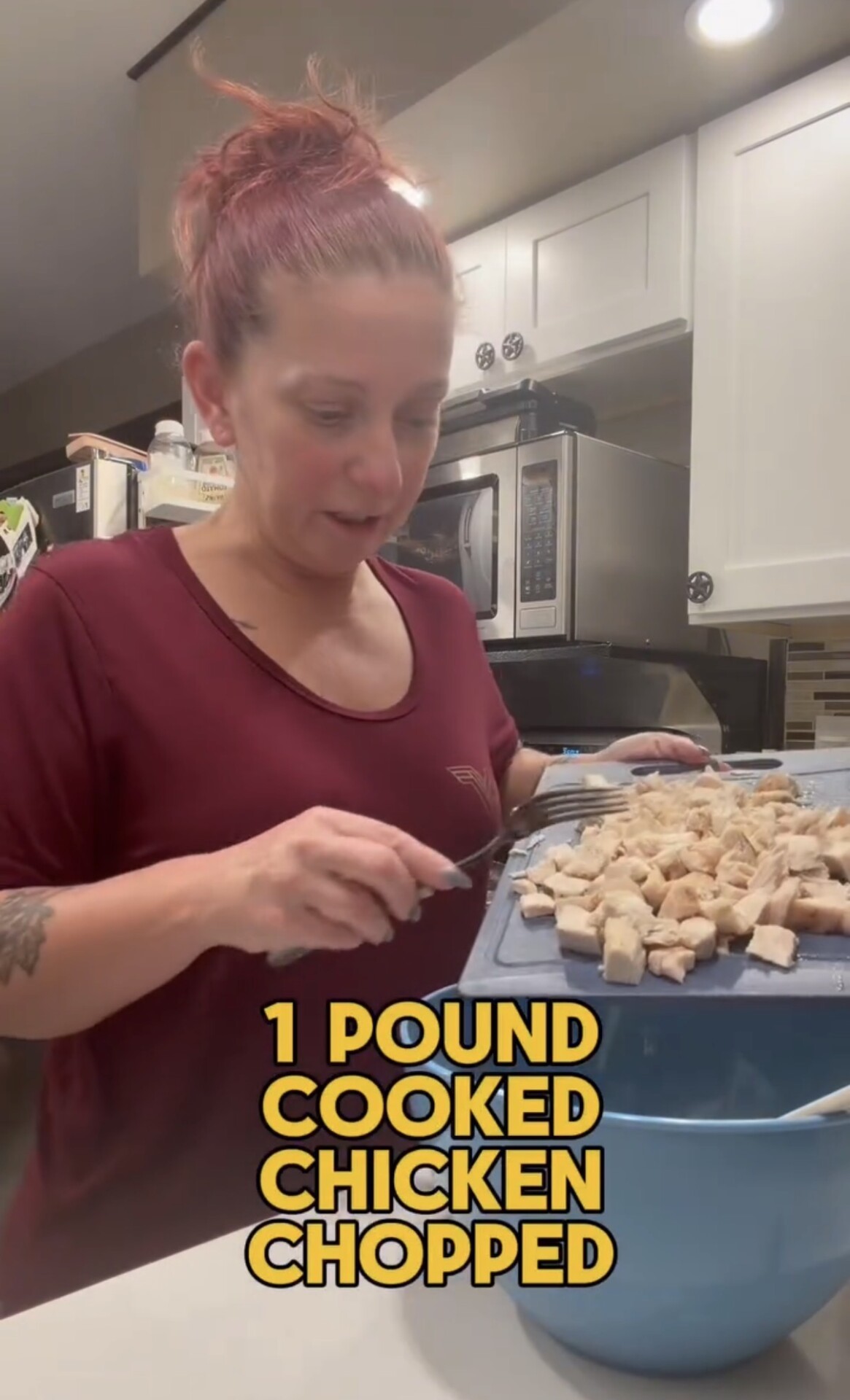 A person uses a fork to scrape chopped, cooked chicken from a cutting board into a large blue bowl, with text overlay reading 1 POUND COOKED CHICKEN CHOPPED.