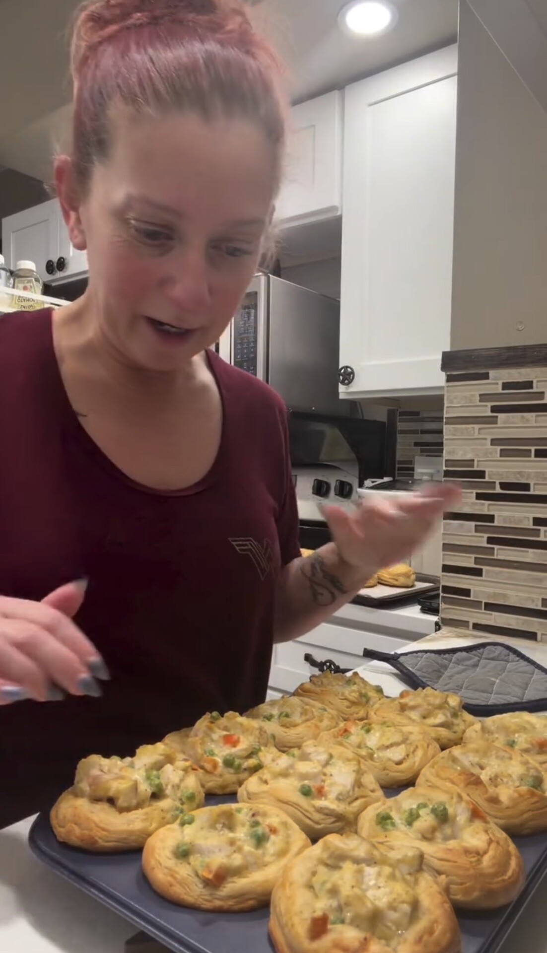 A person holds a baking sheet filled with golden-brown savory puff pastry cups topped with a creamy chicken and vegetable mixture.