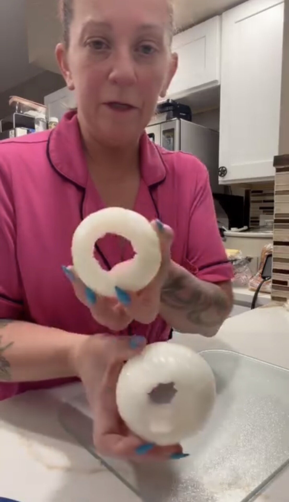 A woman in pink pajamas holds two halves of a peeled onion, each with the center removed.