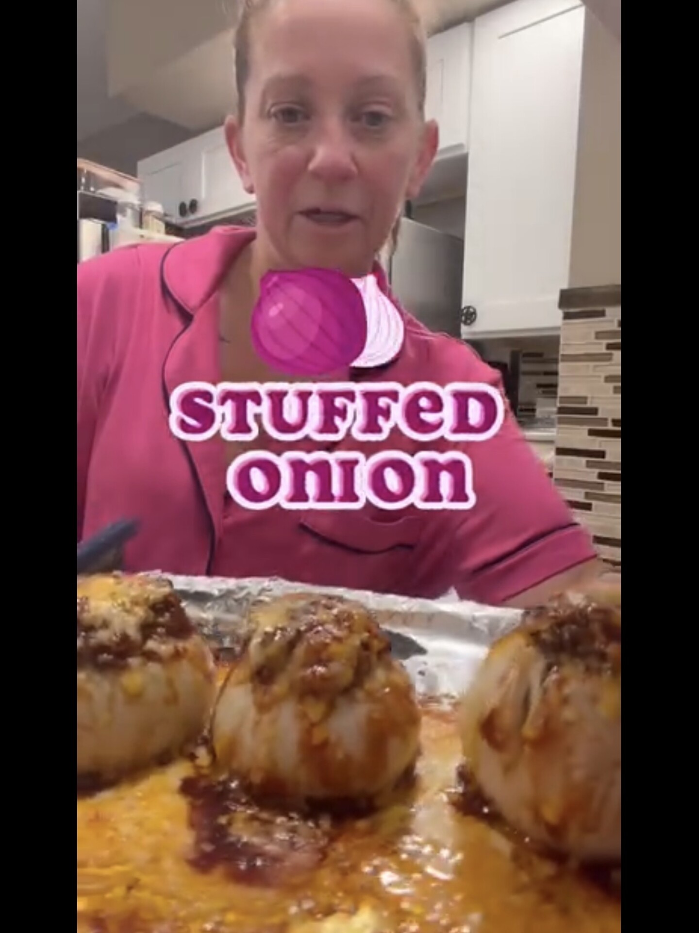 A woman in a pink pajama top presents a baking sheet of baked stuffed onions topped with melted cheese, with a text overlay reading STUFFED onion and an onion icon.