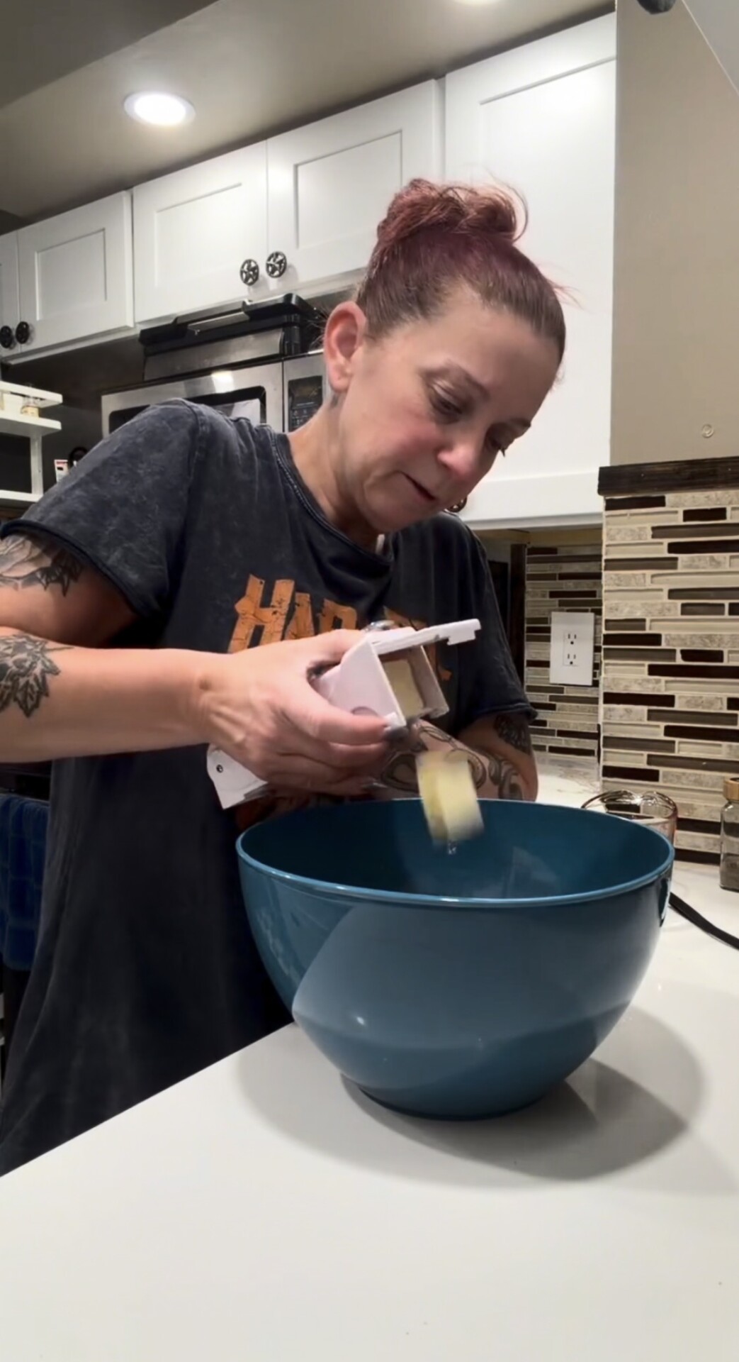 A woman uses a handheld butter slicer to drop pats of butter into a large blue mixing bowl.