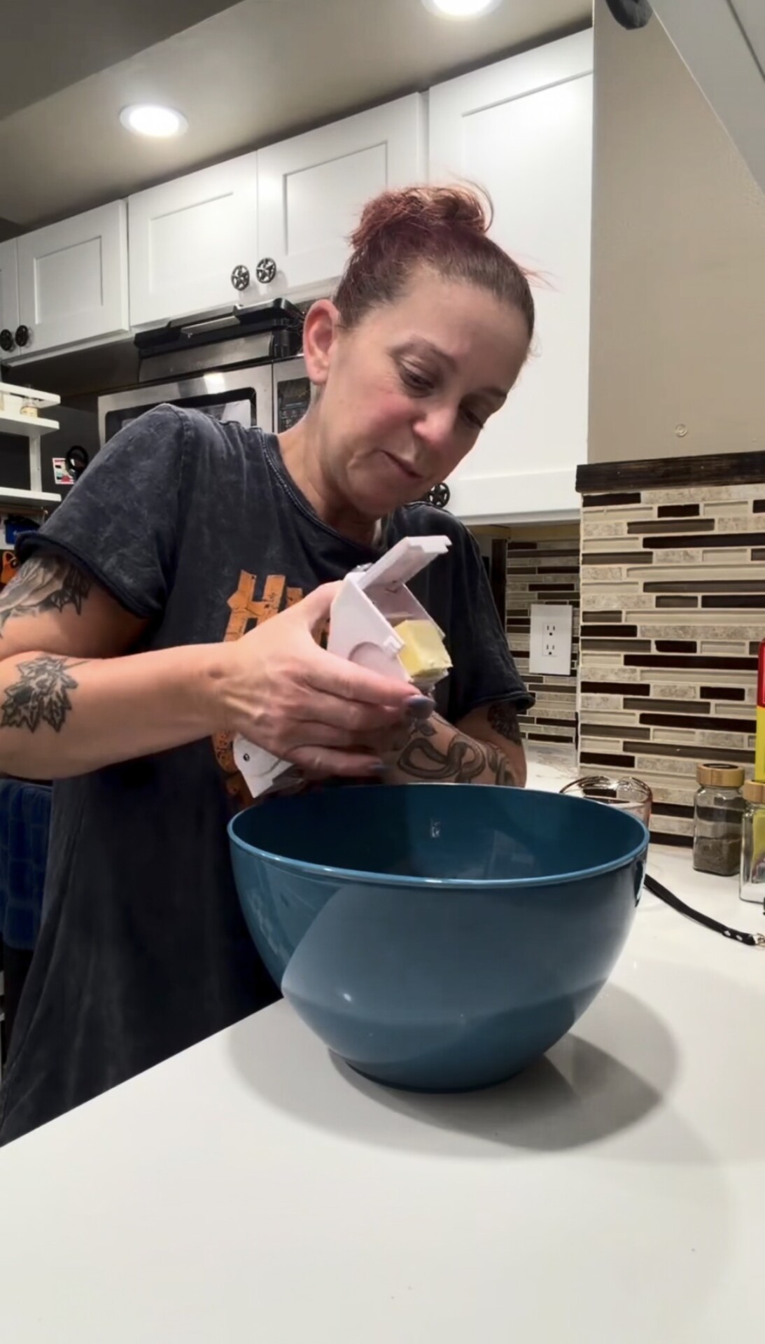 A person uses a butter cutter to slice a stick of butter into a blue mixing bowl.