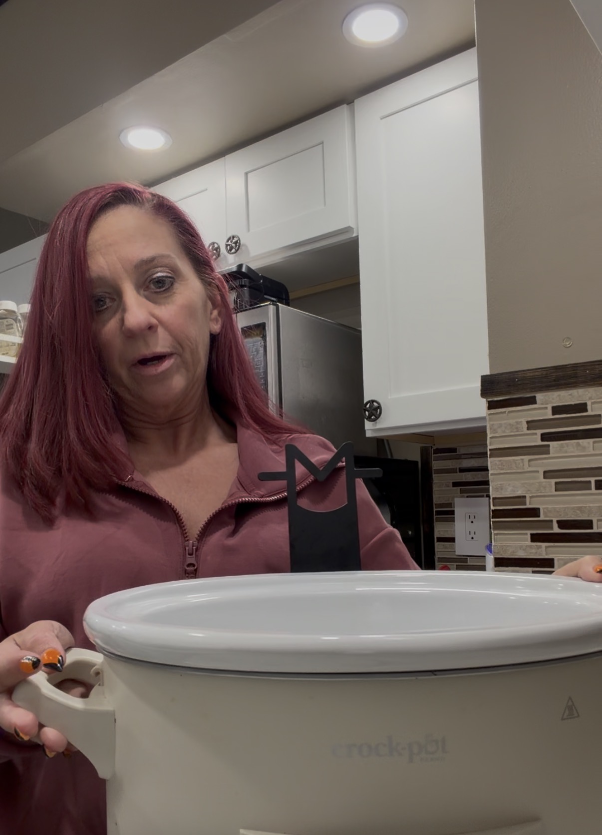 A woman holding a white Crock-Pot ceramic insert with a black metal kitchen tool attached to the rim.