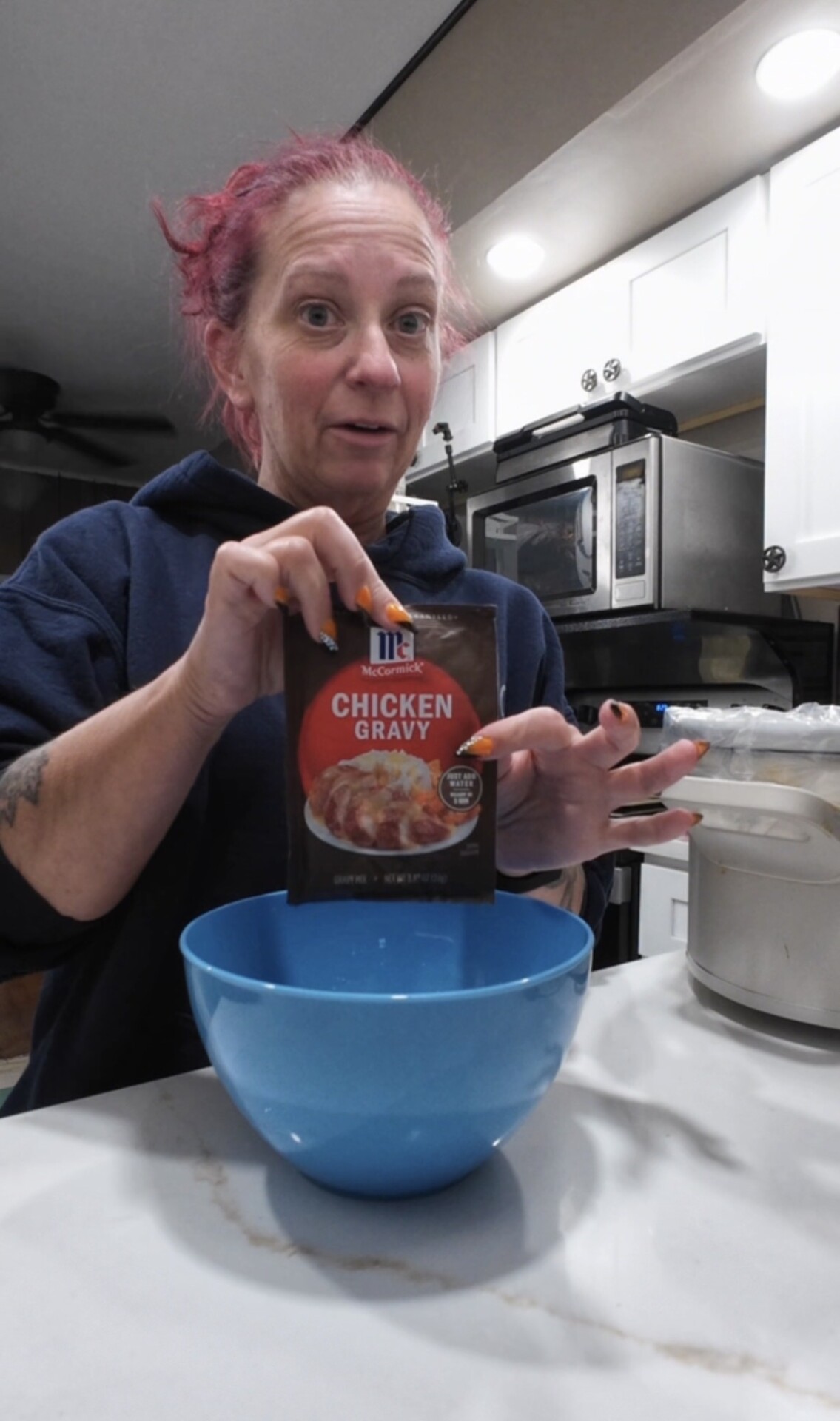 A woman holding a packet of McCormick chicken gravy mix over a blue bowl.