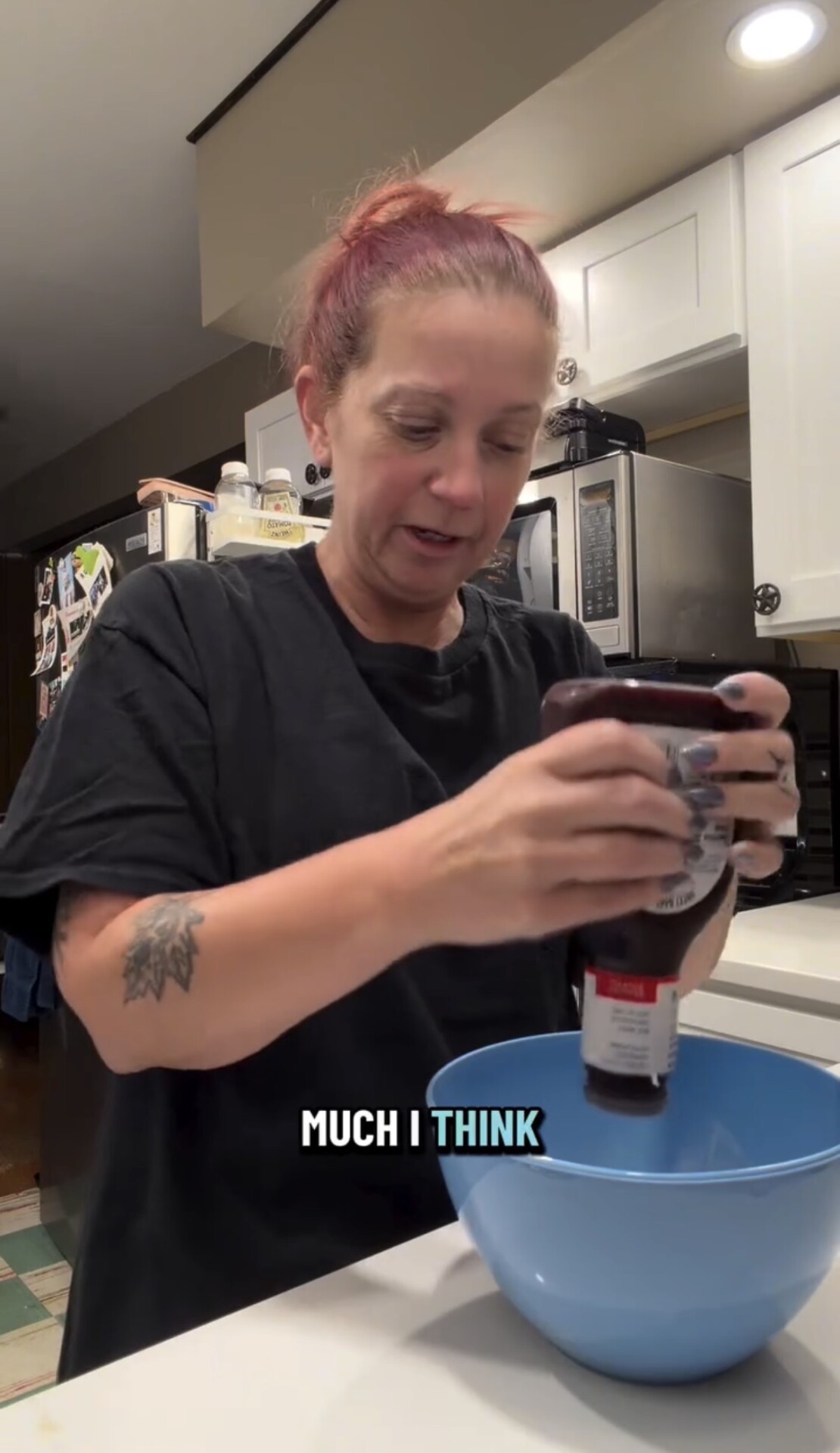 A woman in a black t-shirt squeezes a bottle of barbecue sauce into a blue bowl.