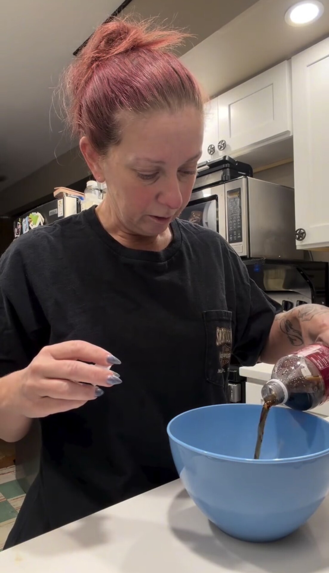 A person pours dark liquid from a plastic bottle into a blue mixing bowl.