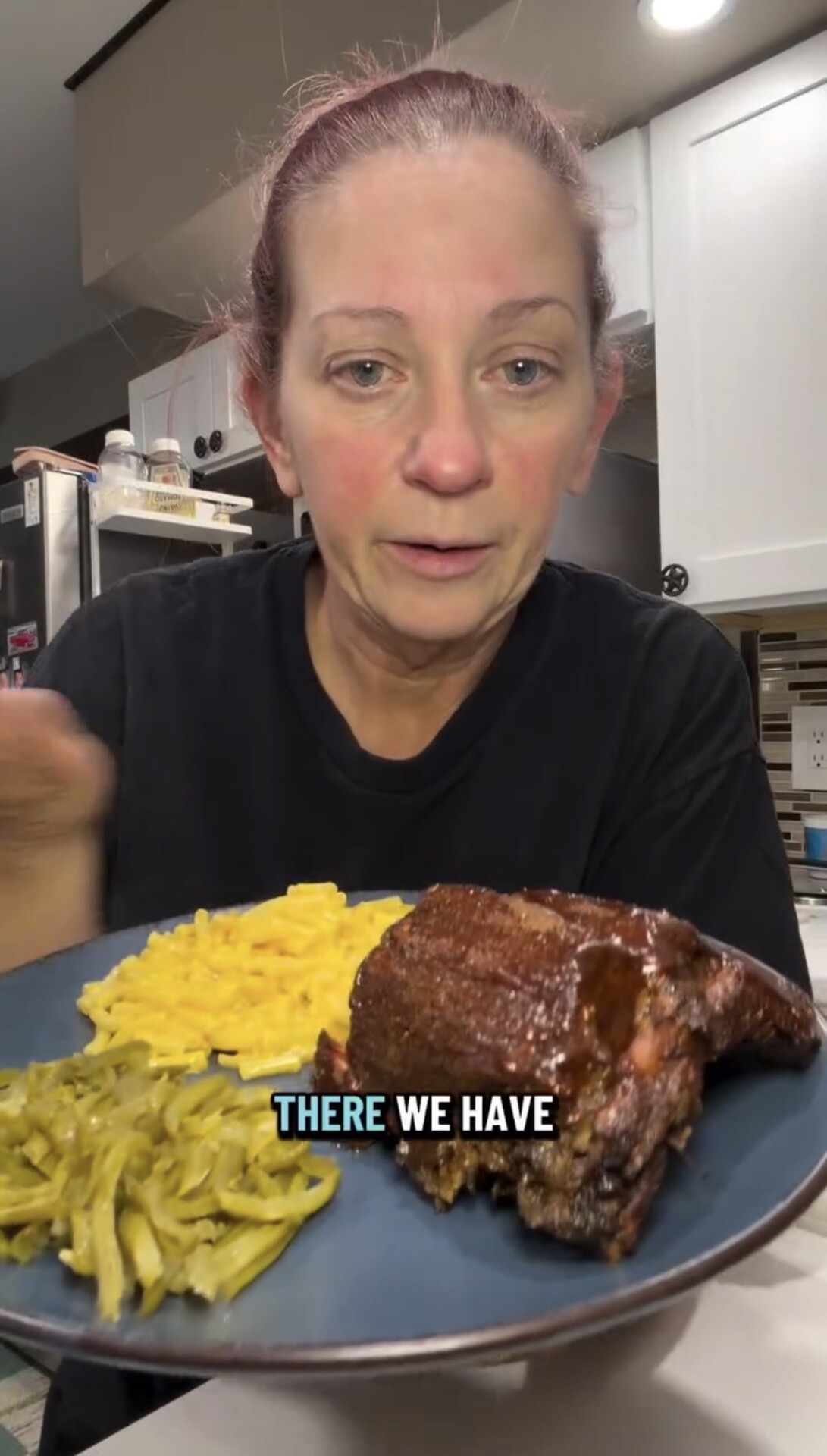 A person holds a plate containing a portion of ribs, macaroni and cheese, and green beans, with the text overlay THERE WE HAVE visible.