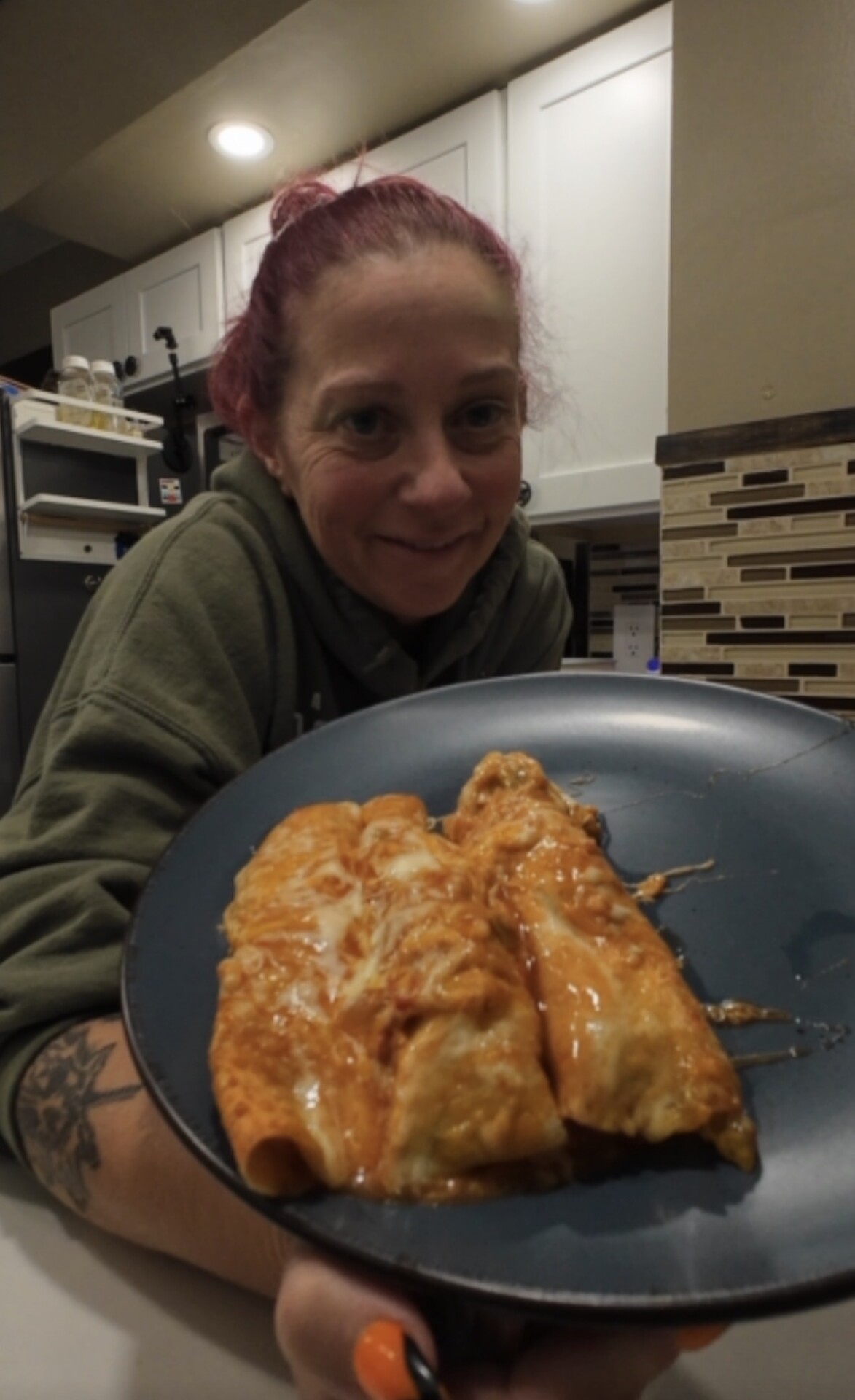 A woman holds a plate with two cheesy enchiladas covered in red sauce.