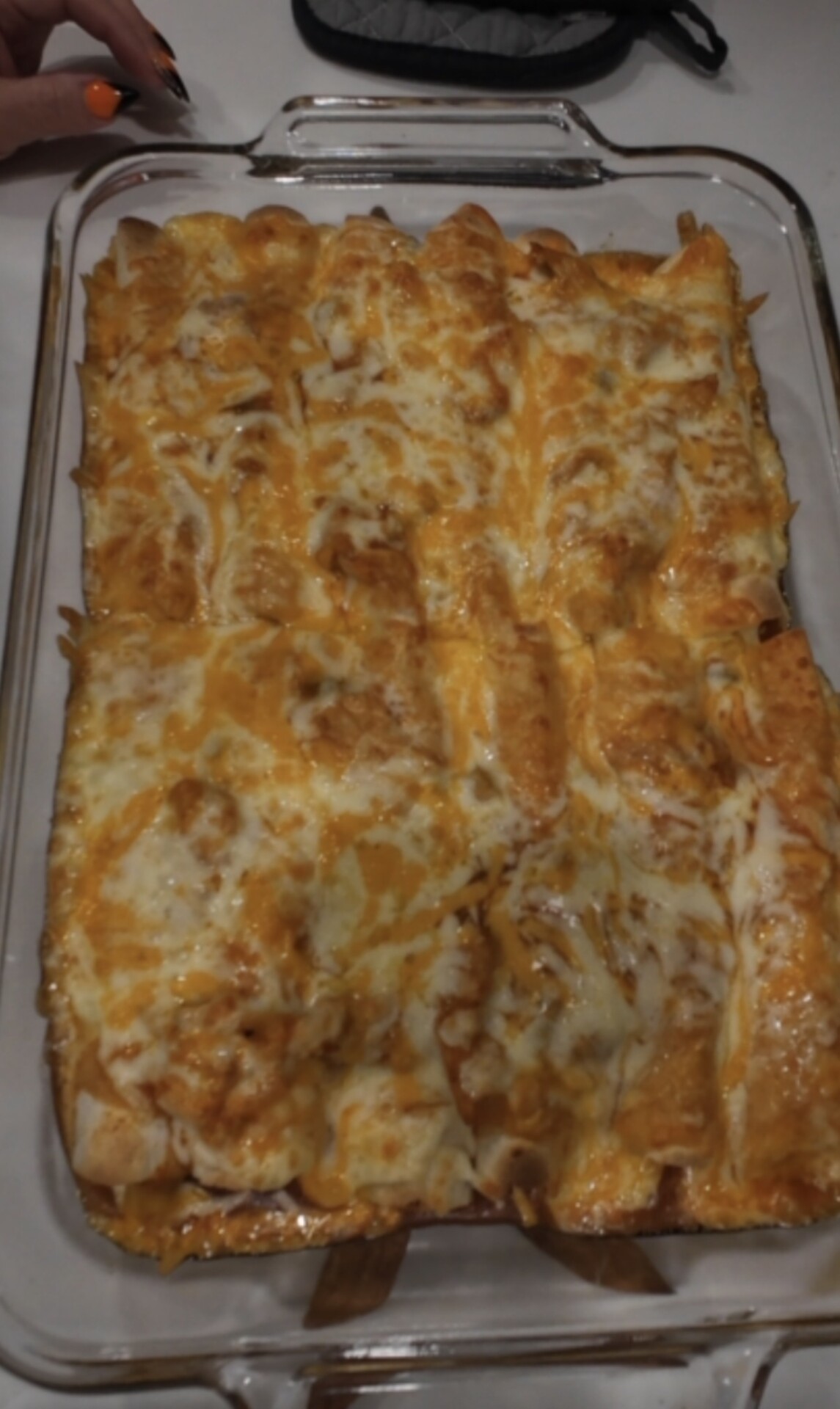 A glass baking dish filled with enchiladas covered in melted cheese.