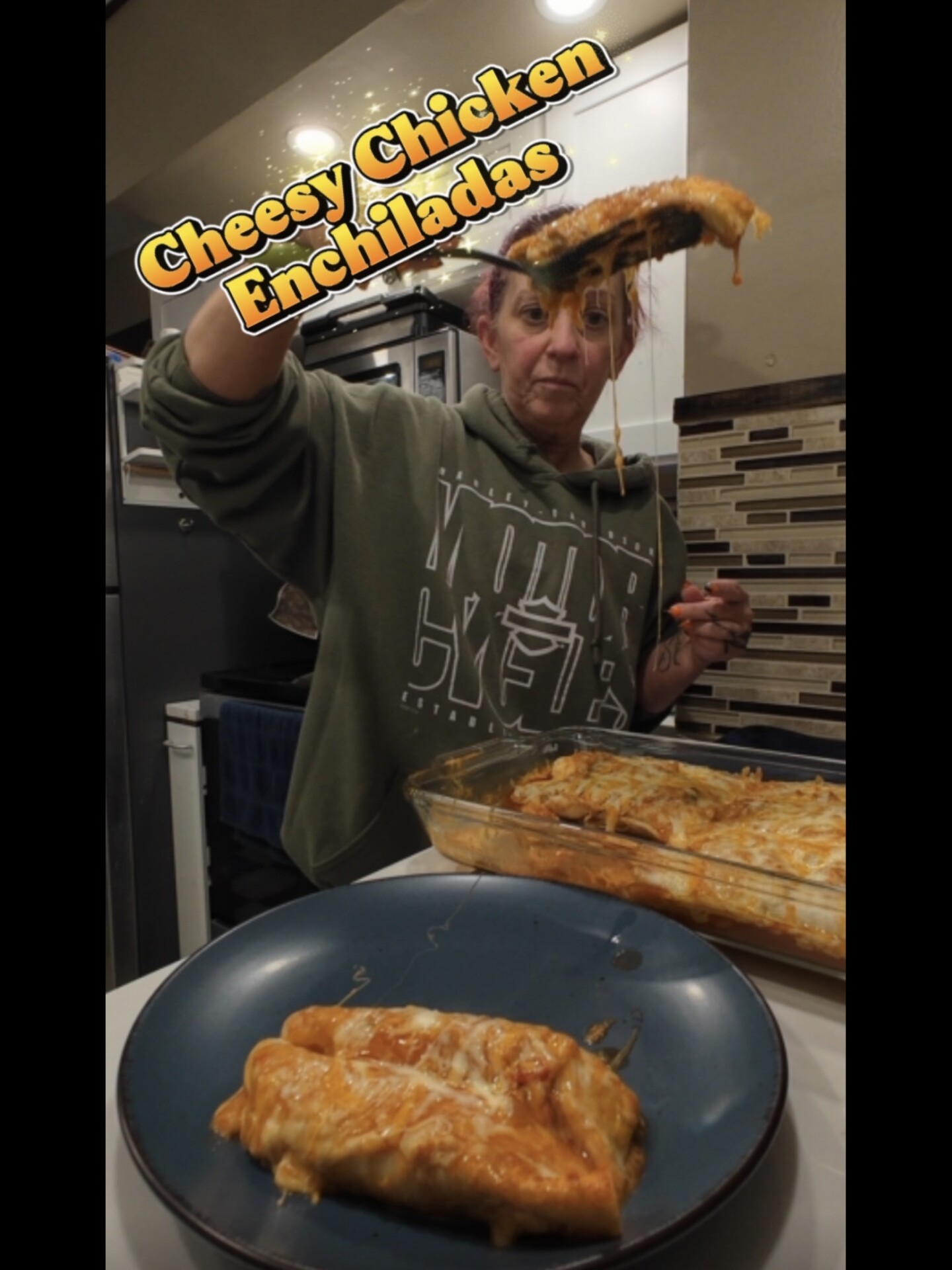A person lifts a cheesy chicken enchilada from a baking dish onto a plate, with text at the top reading Cheesy Chicken Enchiladas.