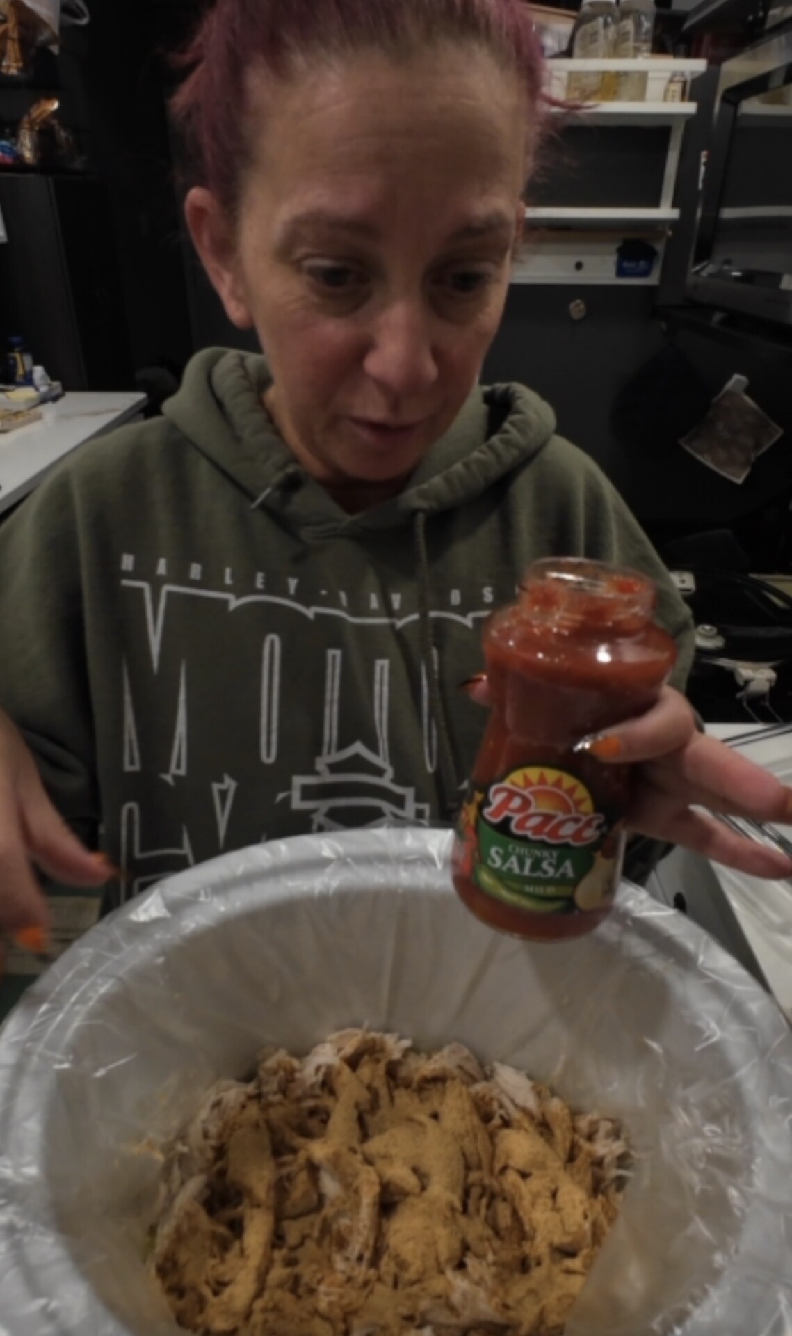 A woman holding a jar of Pace Chunky Salsa over a slow cooker filled with shredded meat.