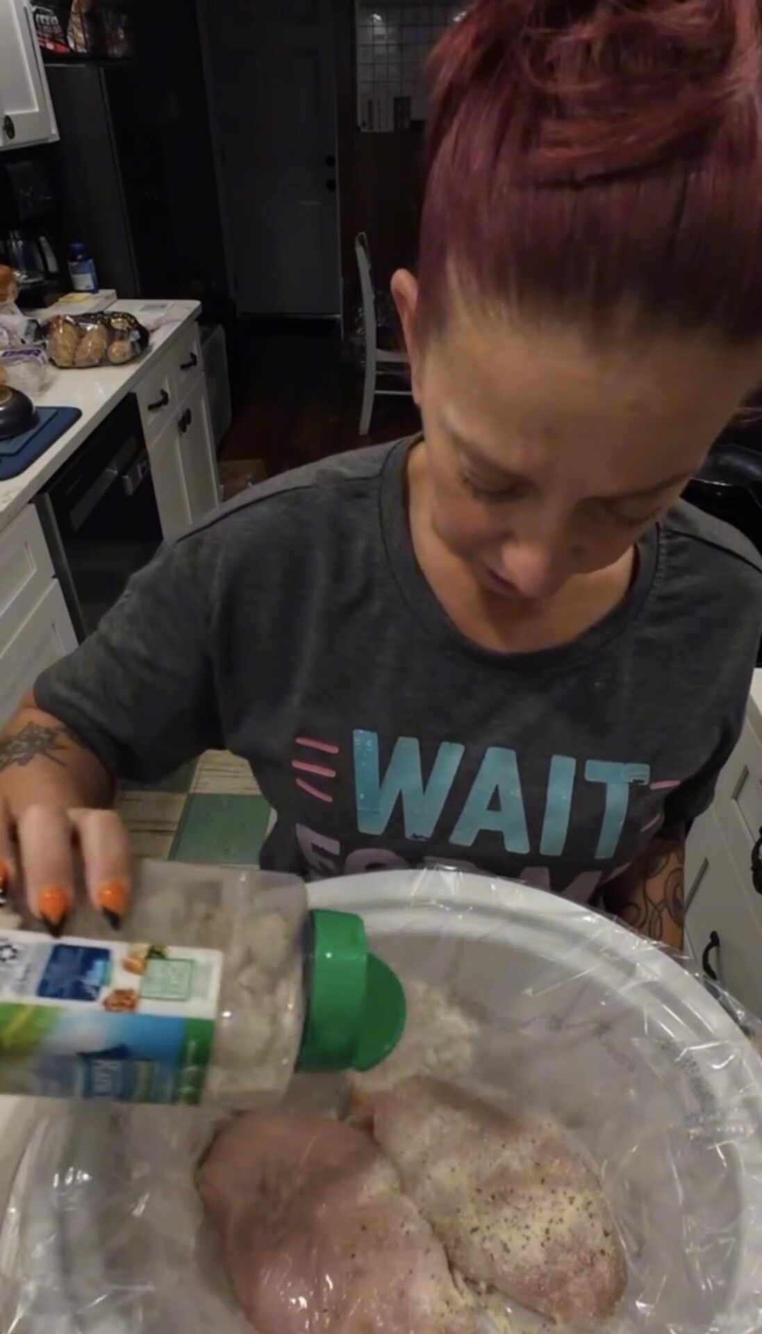 A woman seasoning raw chicken breasts inside a slow cooker.