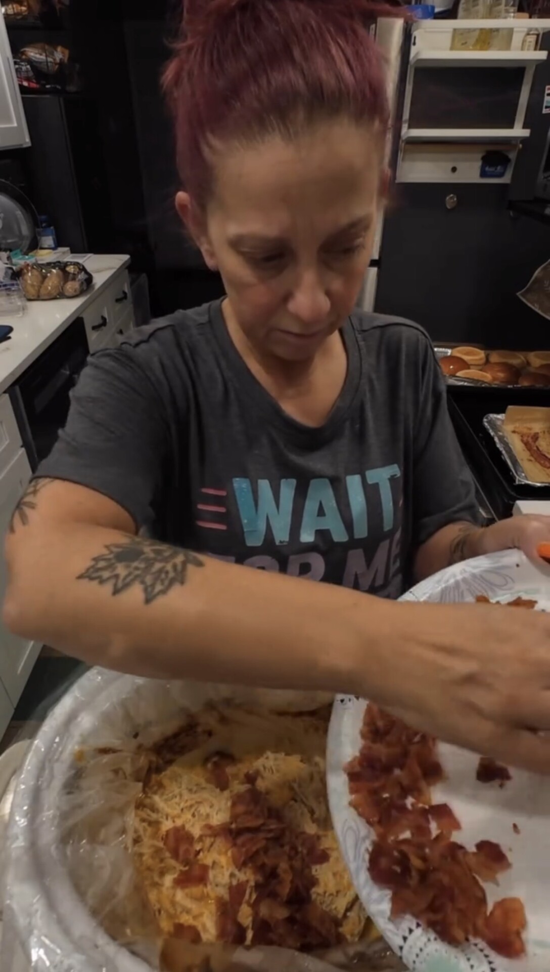 A person in a Wait for Me t-shirt adding crumbled bacon from a paper plate into a slow cooker filled with food.