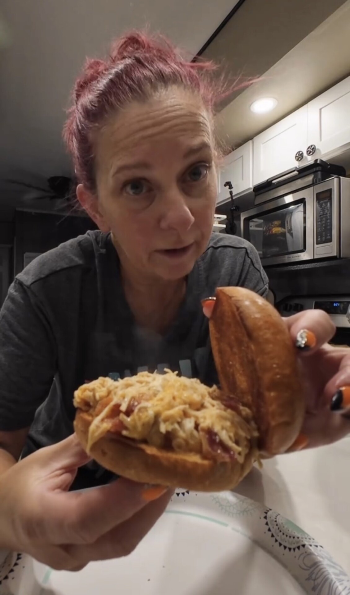 A woman holds open a sandwich filled with shredded meat and melted cheese.