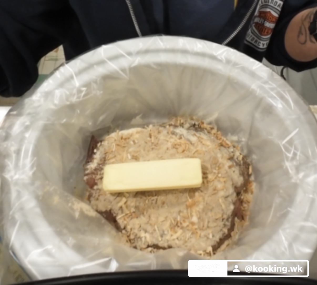A slow cooker lined with a plastic bag contains a breaded food item topped with a stick of butter.