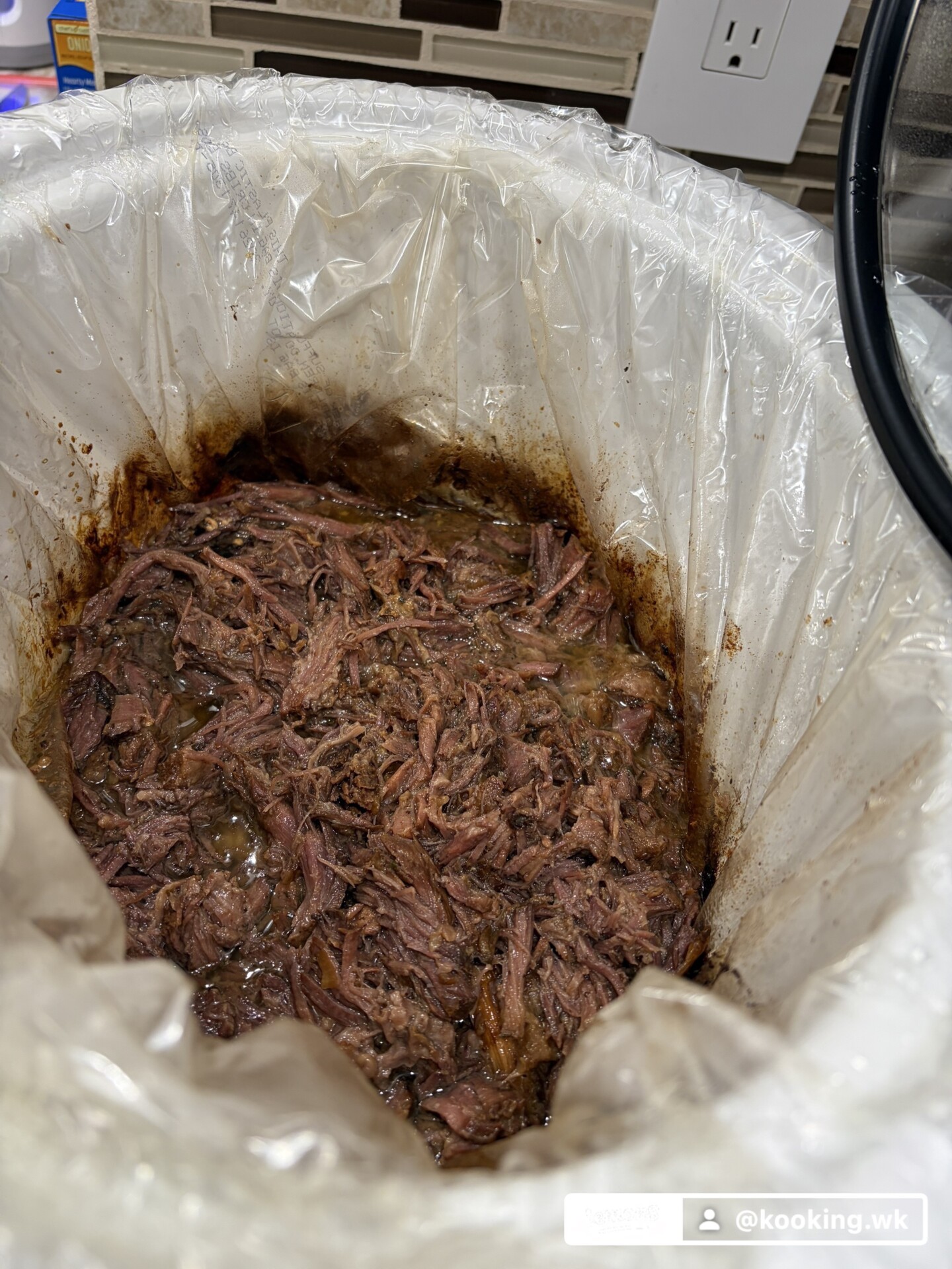 Shredded beef in a slow cooker lined with a plastic bag.
