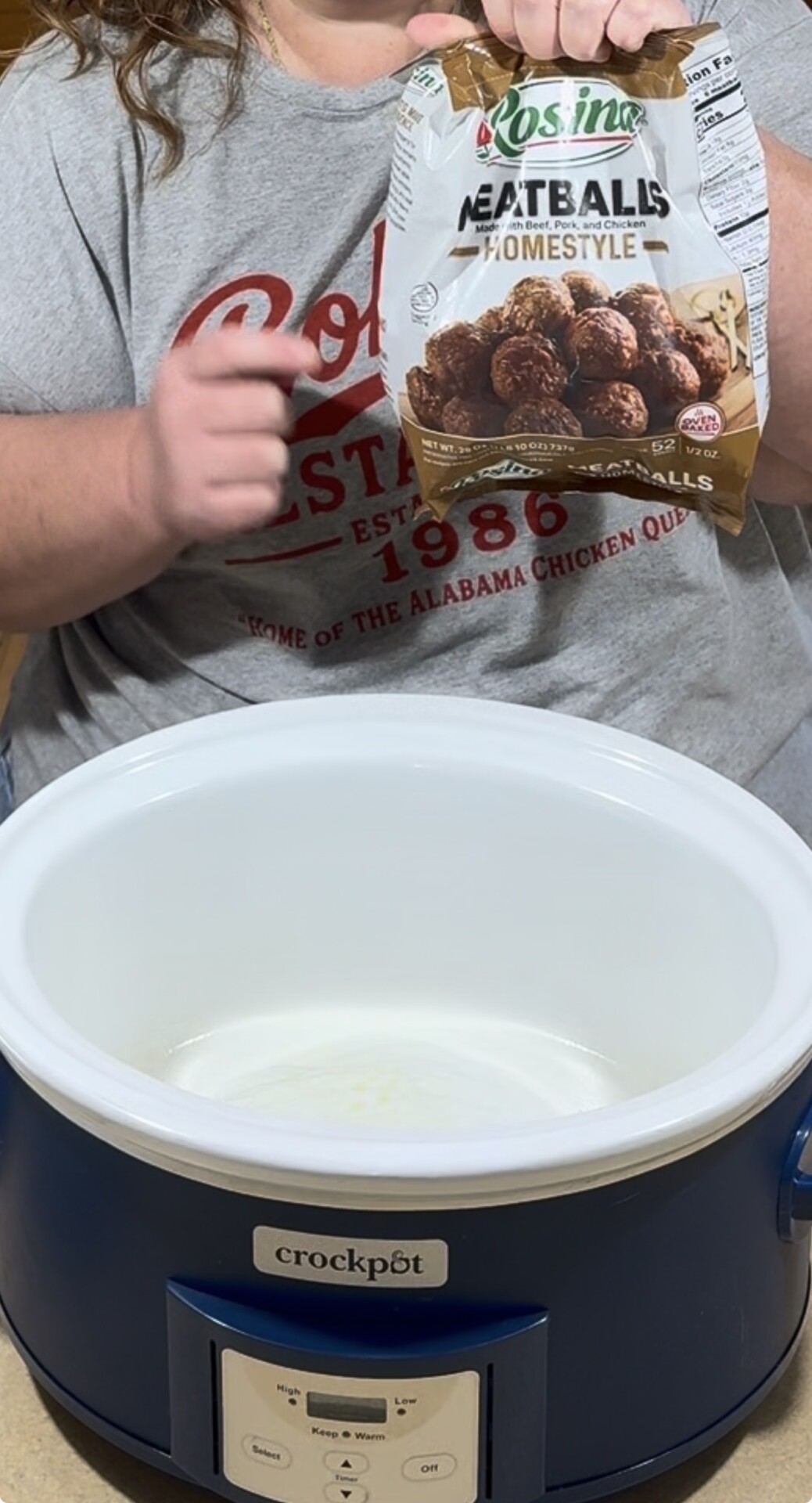 A person holding a bag of Rosina homestyle meatballs over an empty blue and white Crock-Pot.