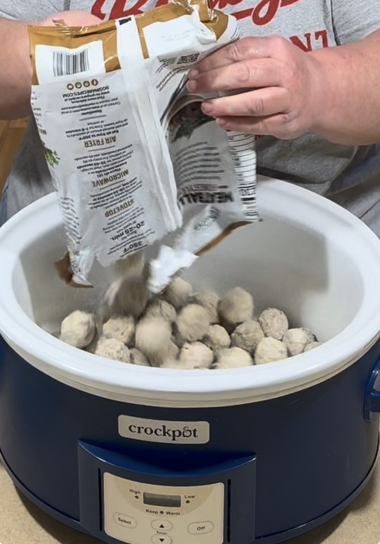 A person pours a bag of frozen meatballs into a blue Crockpot.