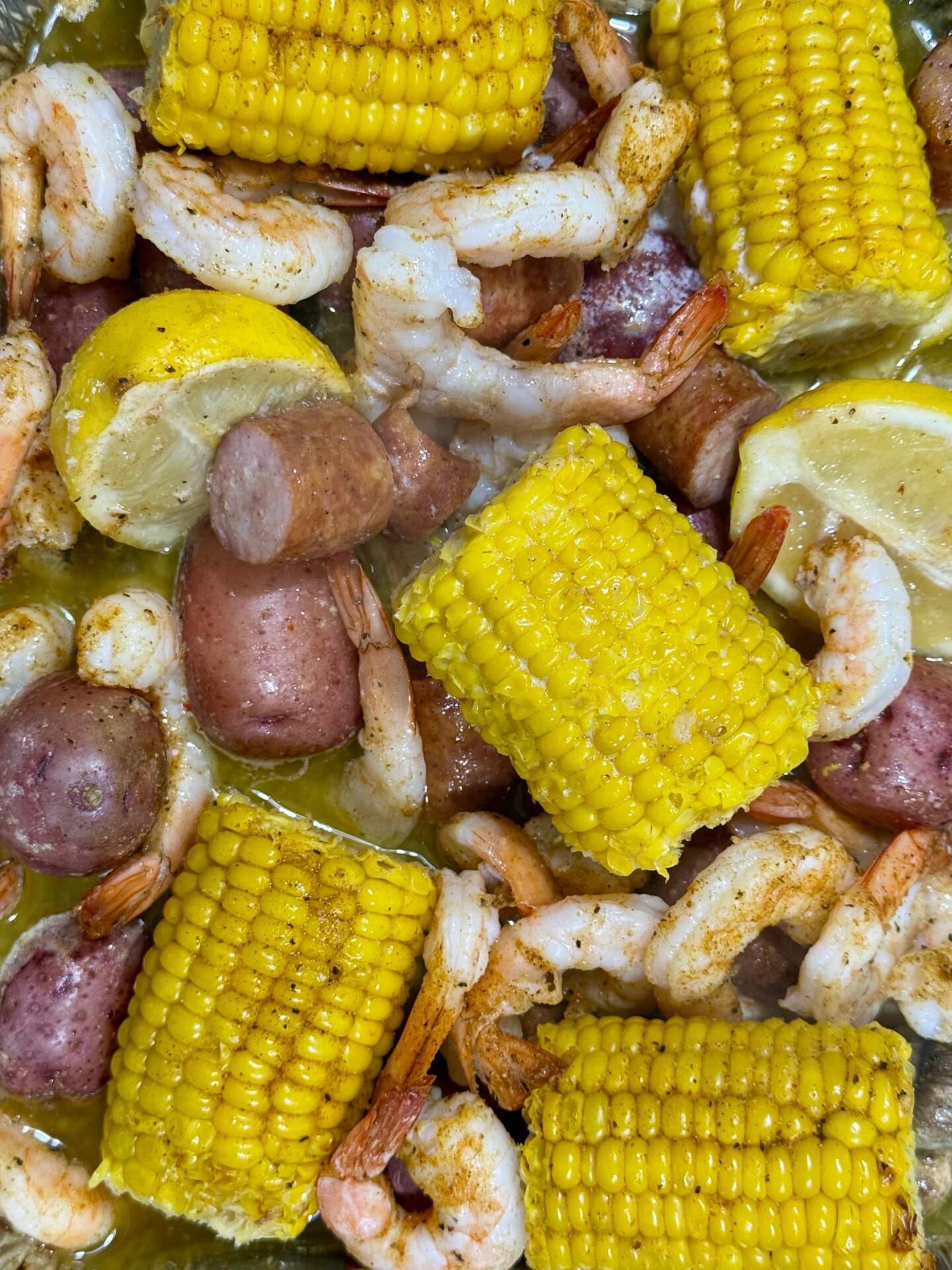 Shrimp boil with corn on the cob, red potatoes, sliced sausage, and lemon wedges in a buttery sauce.