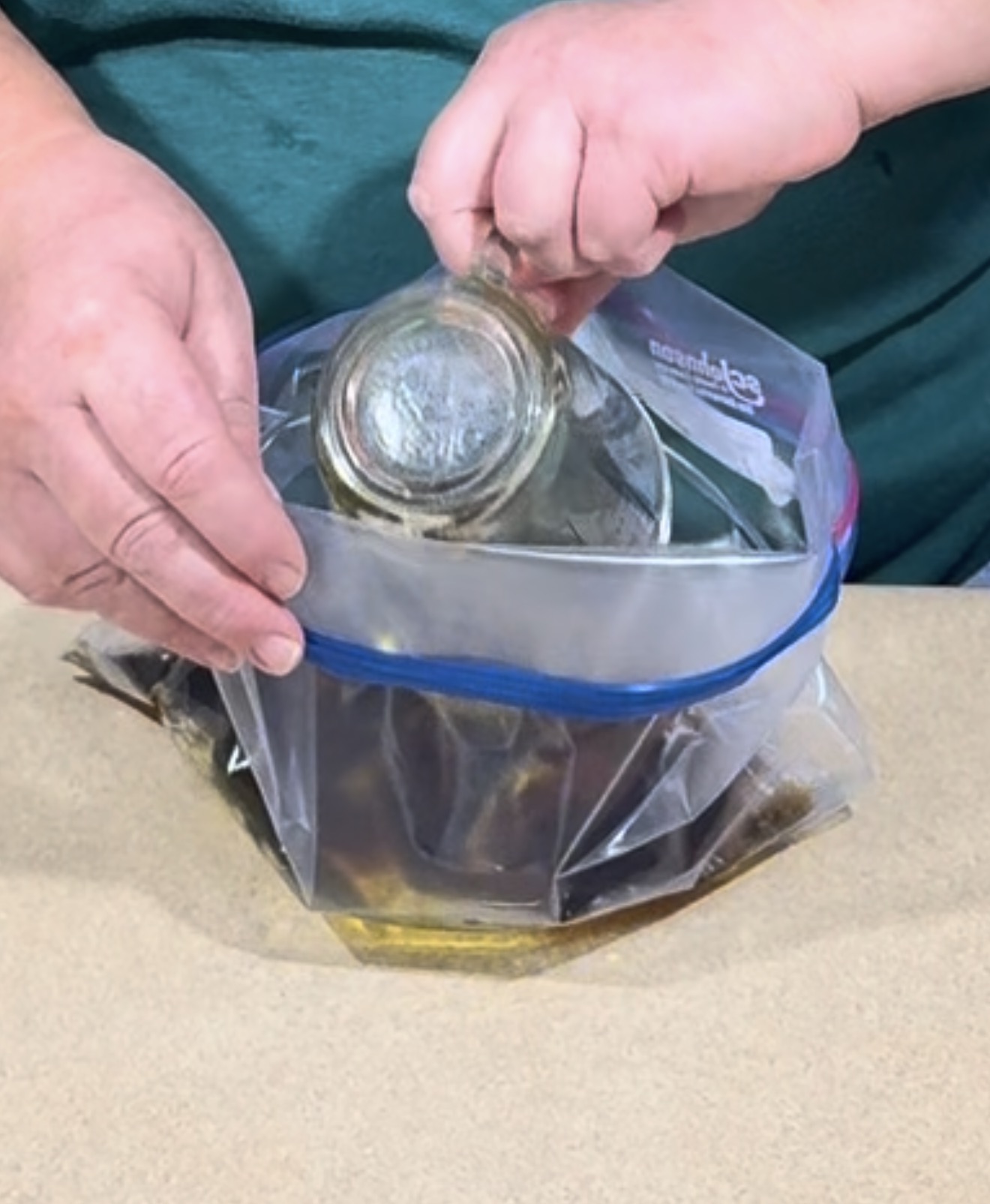 Hands lowering a glass jar into an open plastic storage bag filled with liquid.