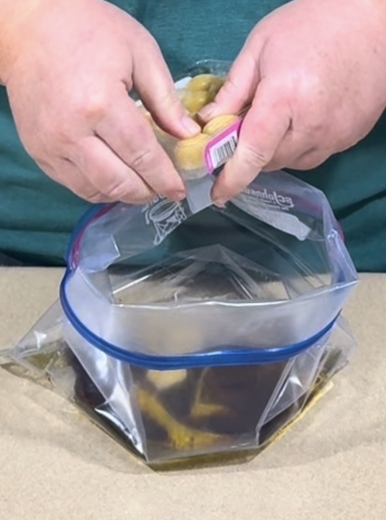 Hands pouring a plastic container of small round food items into a large open freezer bag containing dark liquid.