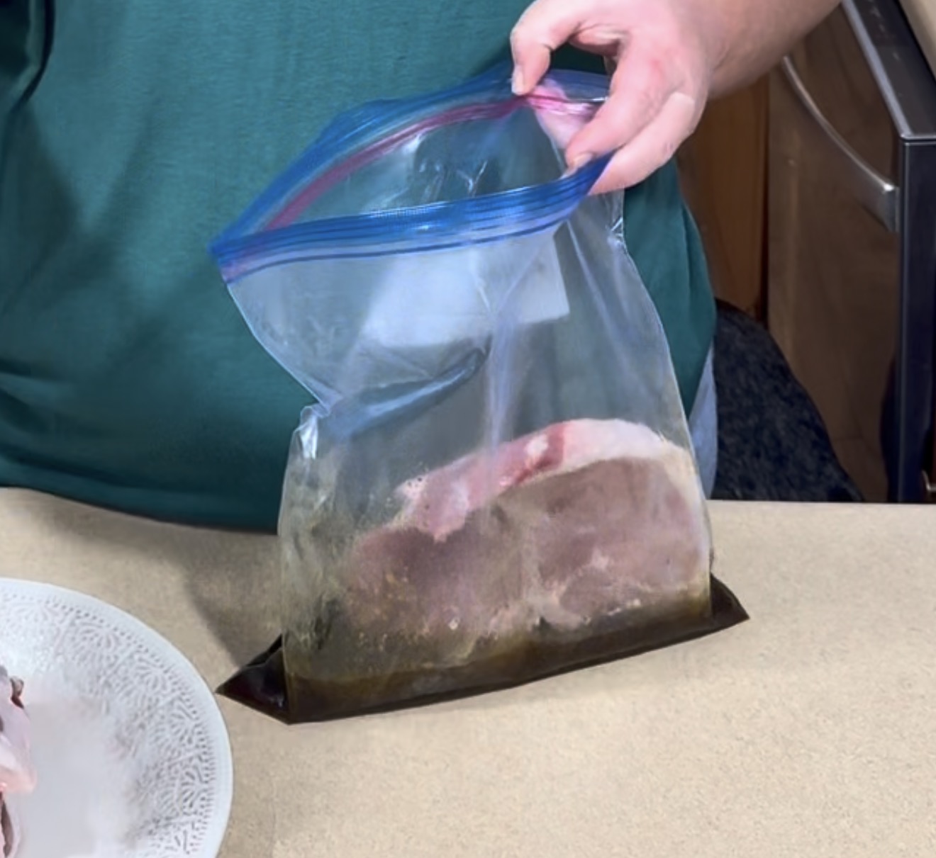 A person places a raw pork chop into a plastic storage bag filled with marinade.